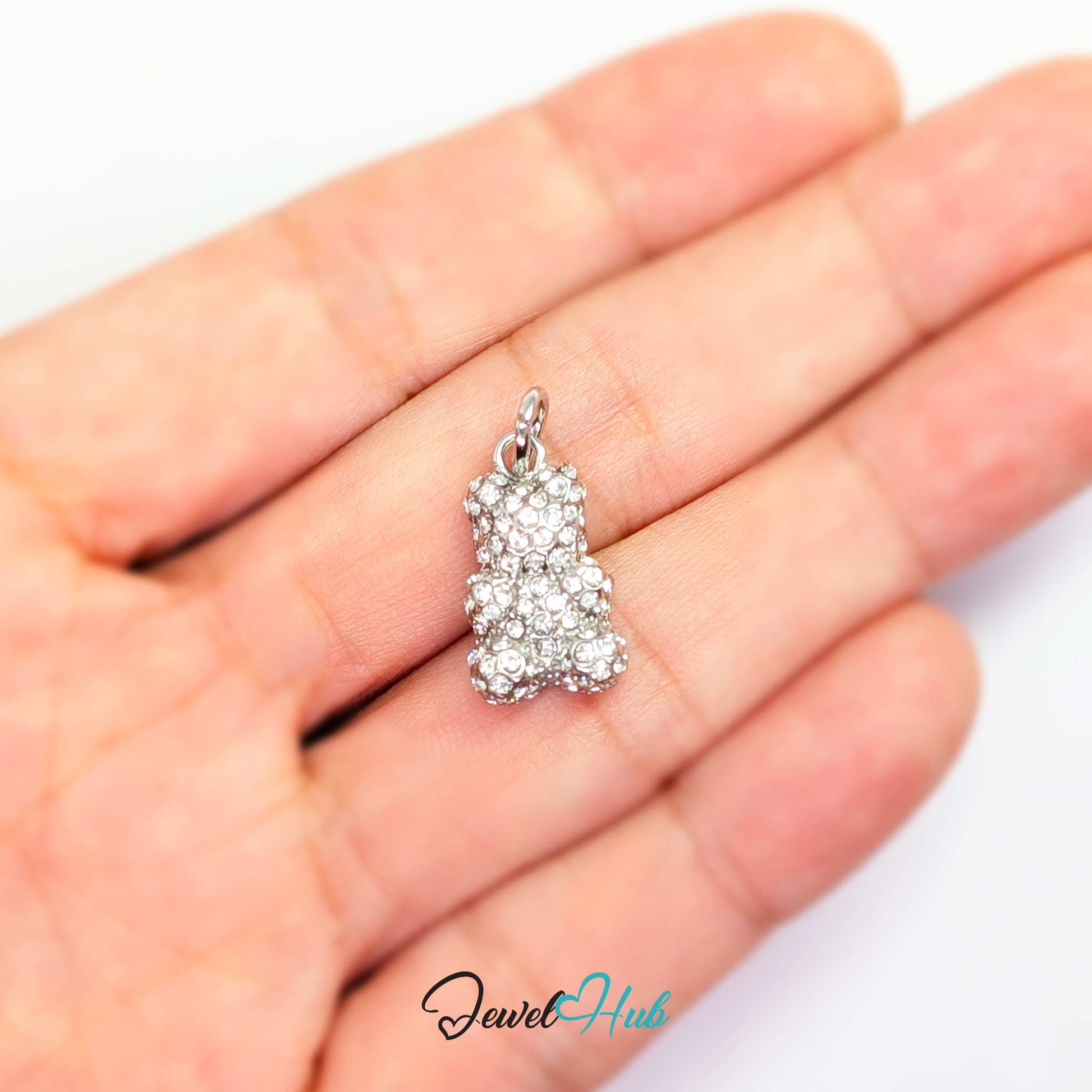 A small silver bear-shaped pendant covered in clear rhinestones, resting on an open hand against a white background. A 'JewelHub' watermark is visible at the bottom.