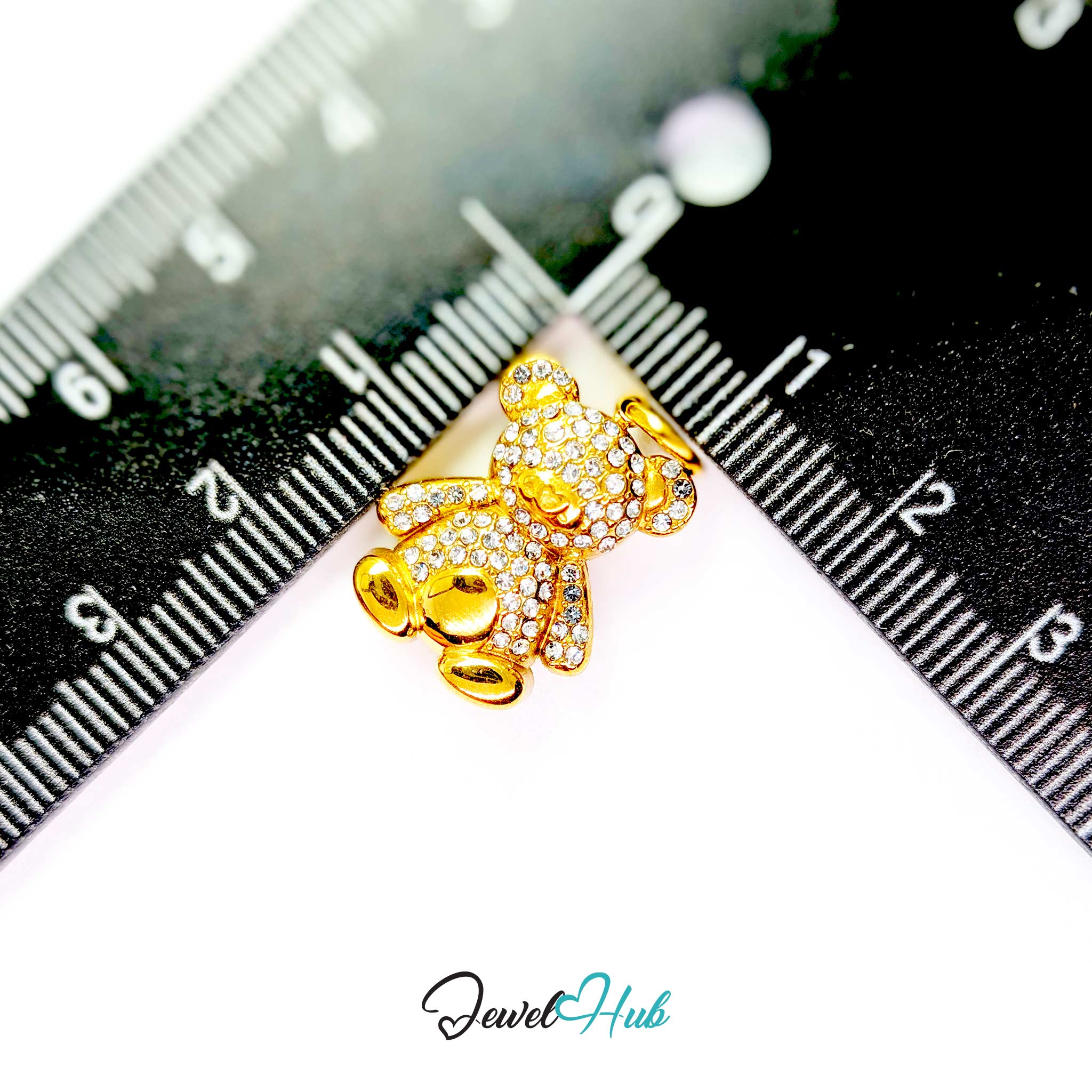 A gold teddy bear charm covered with small clear rhinestones, shown on a white background with a black ruler for scale and a JewelHub logo at the bottom.
