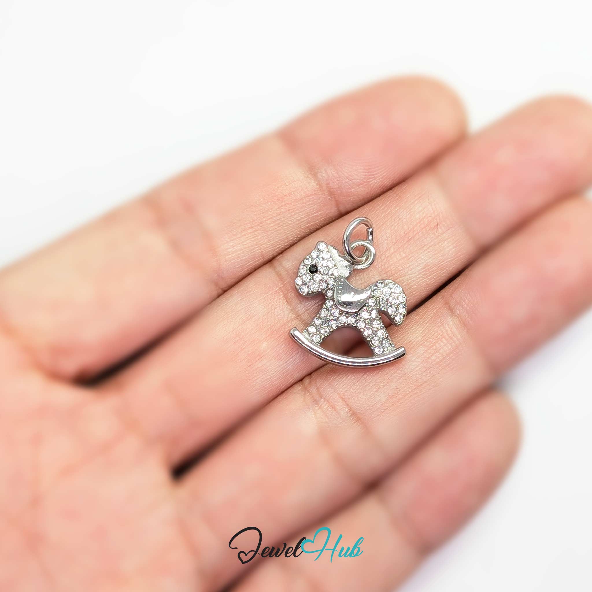 Silver rocking horse charm held in the hand to show its size against a fingertip - JewelHub