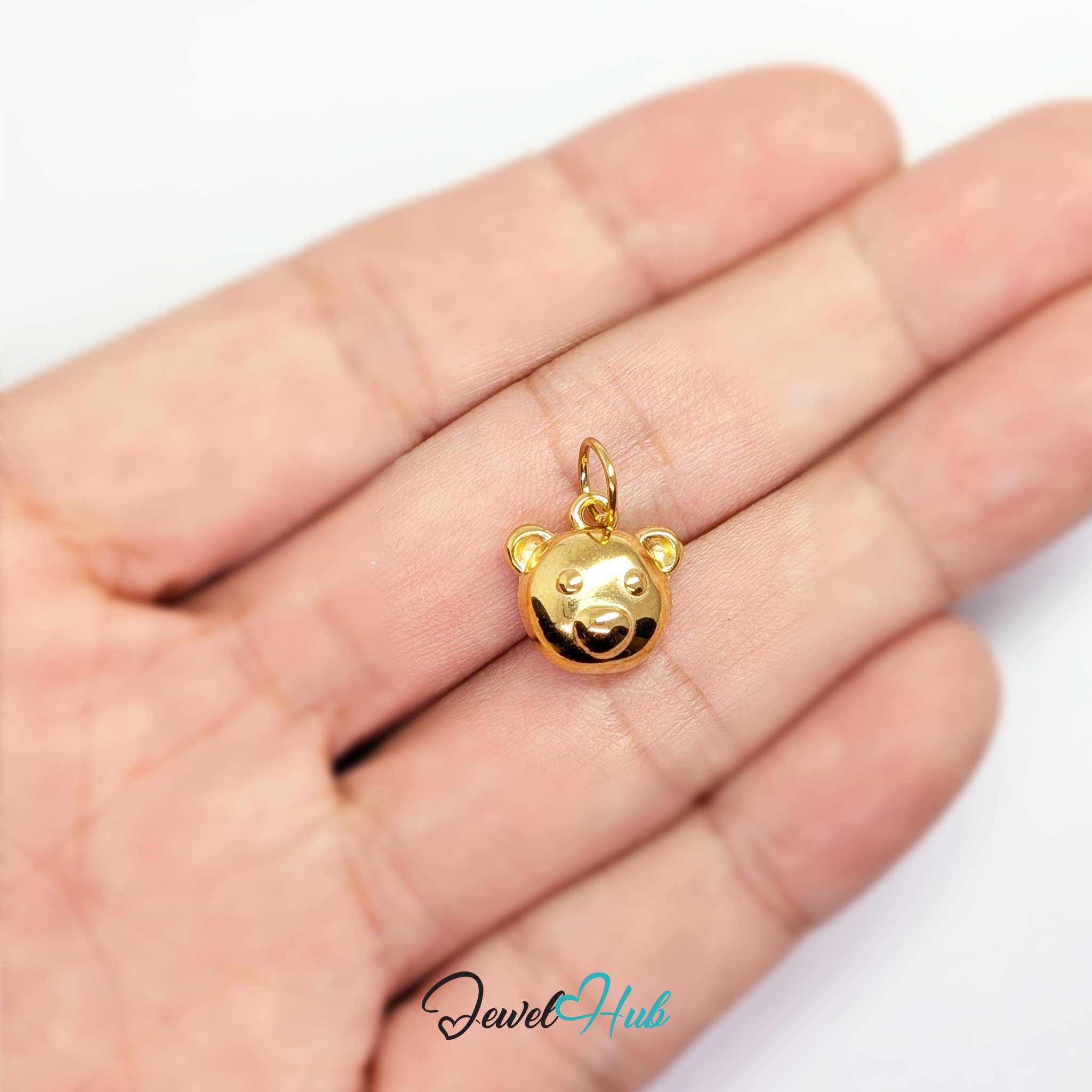 Gold bear head charm held in the hand to show its size against a fingertip - JewelHub