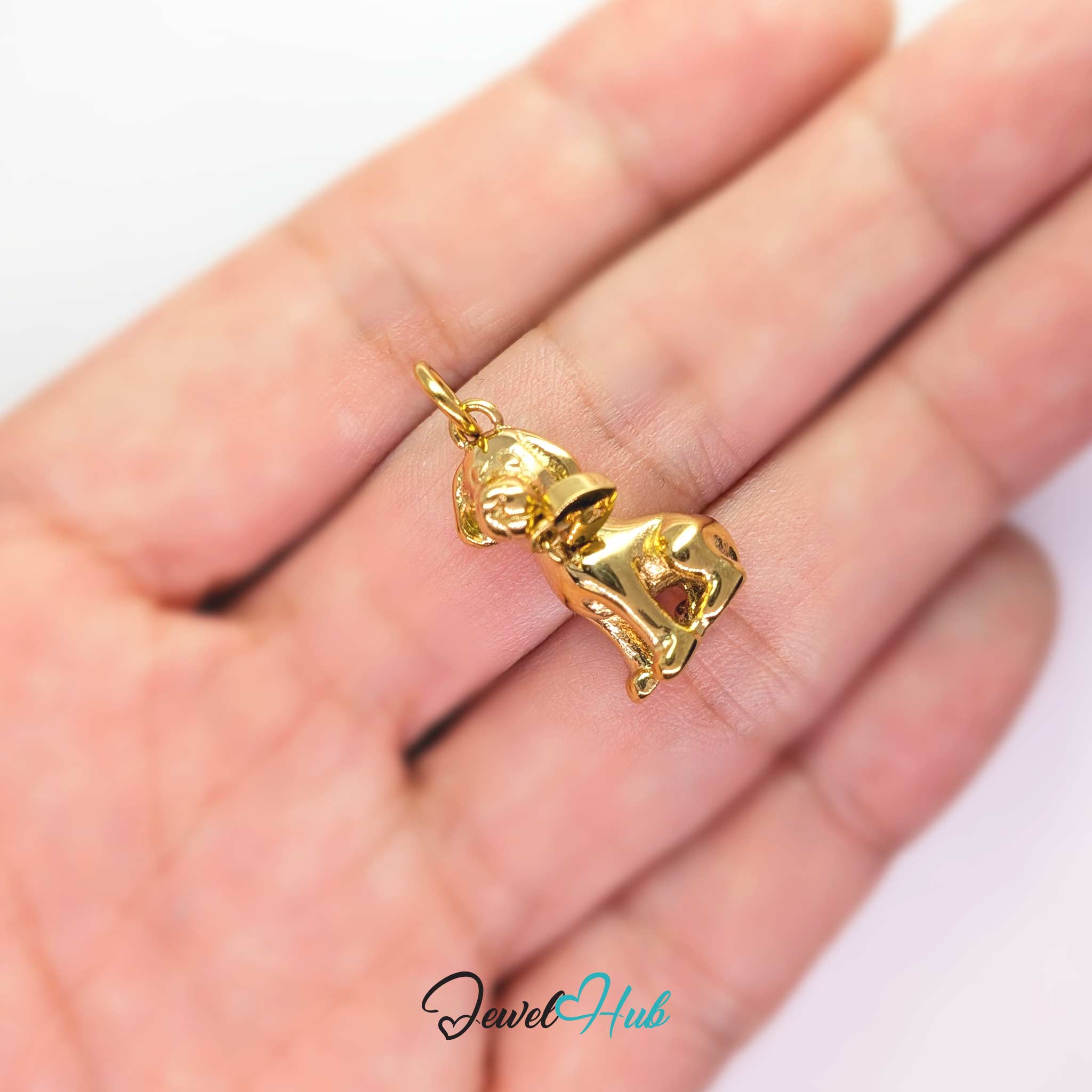 Gold sitting puppy charm held in the hand to show its size against a fingertip - JewelHub