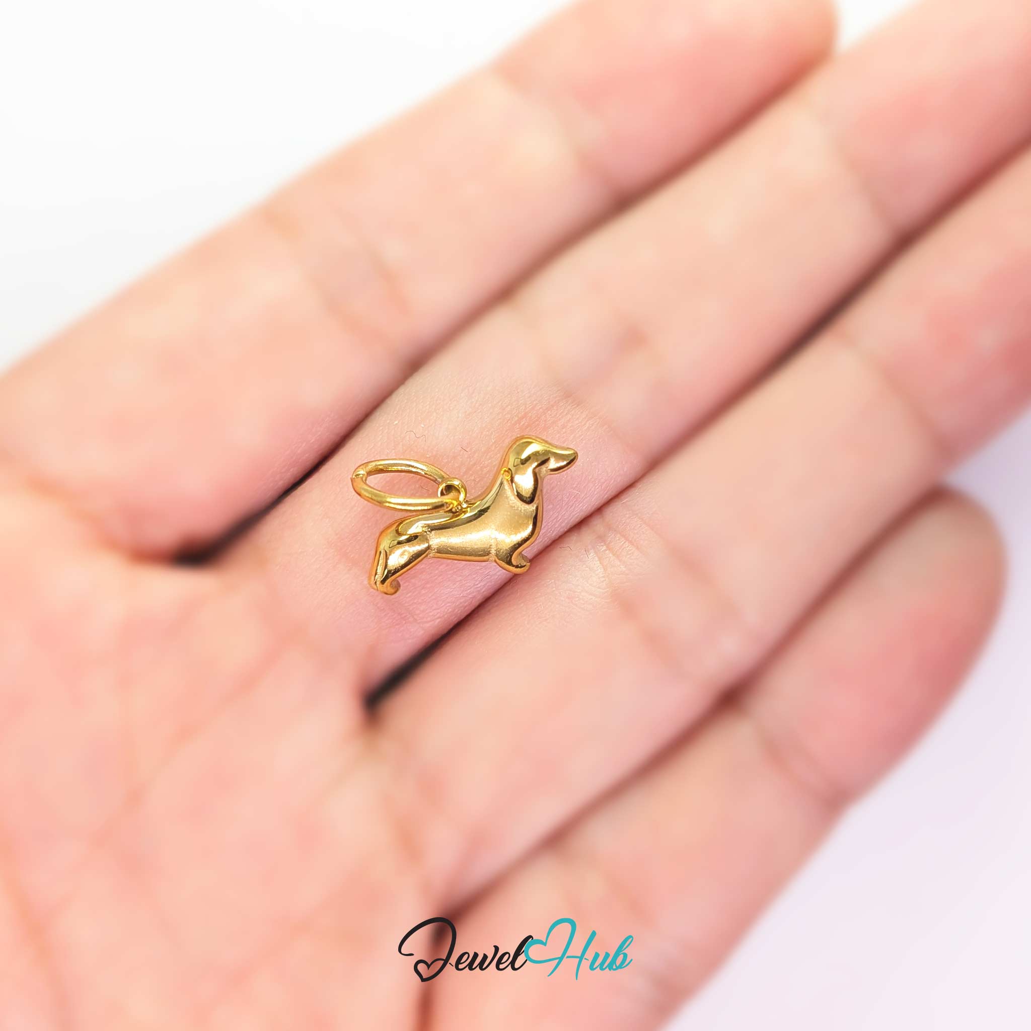 Gold dachshund charm held in the hand to show its size against a fingertip - JewelHub