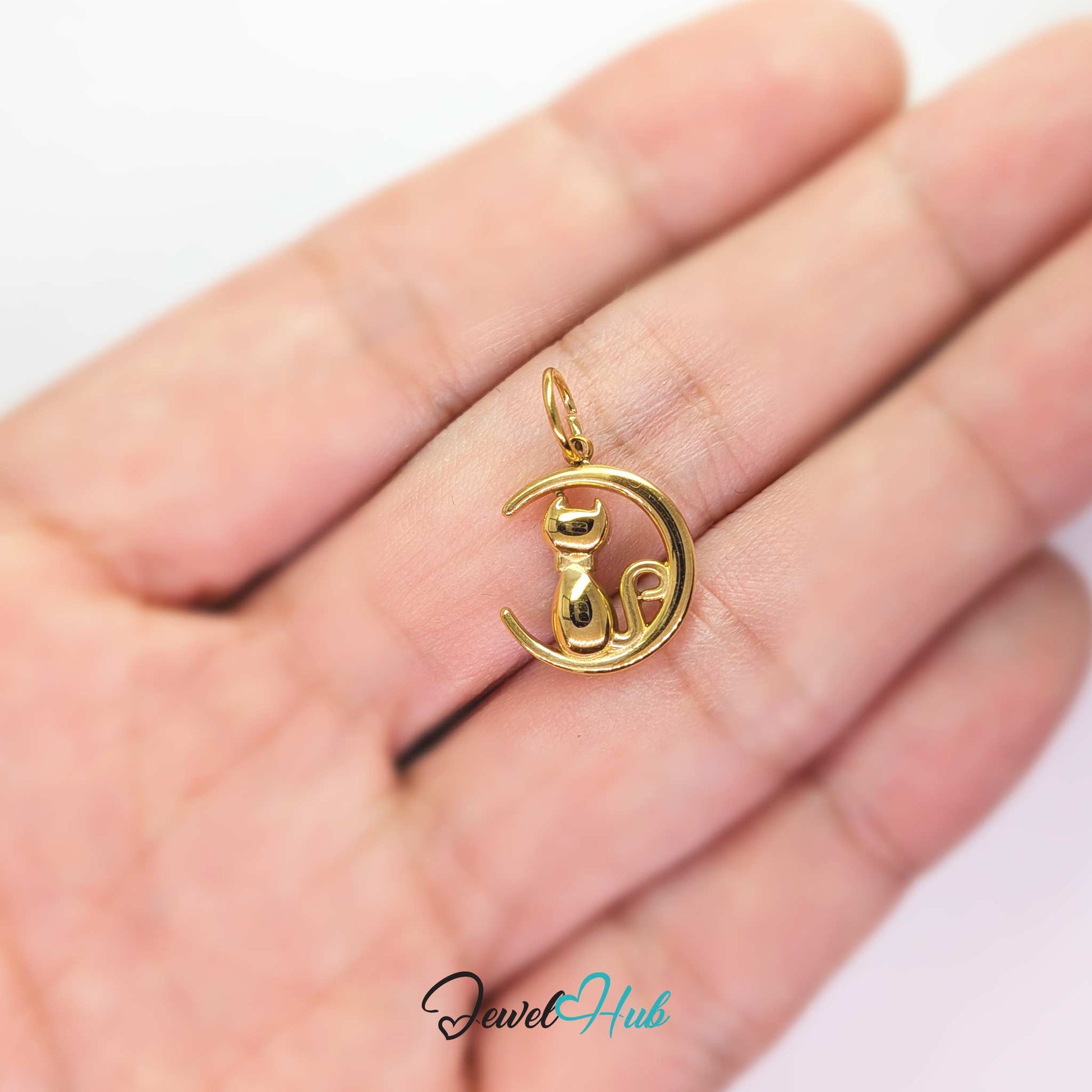 Gold cat and moon charm held in the hand to show its size against a fingertip - JewelHub