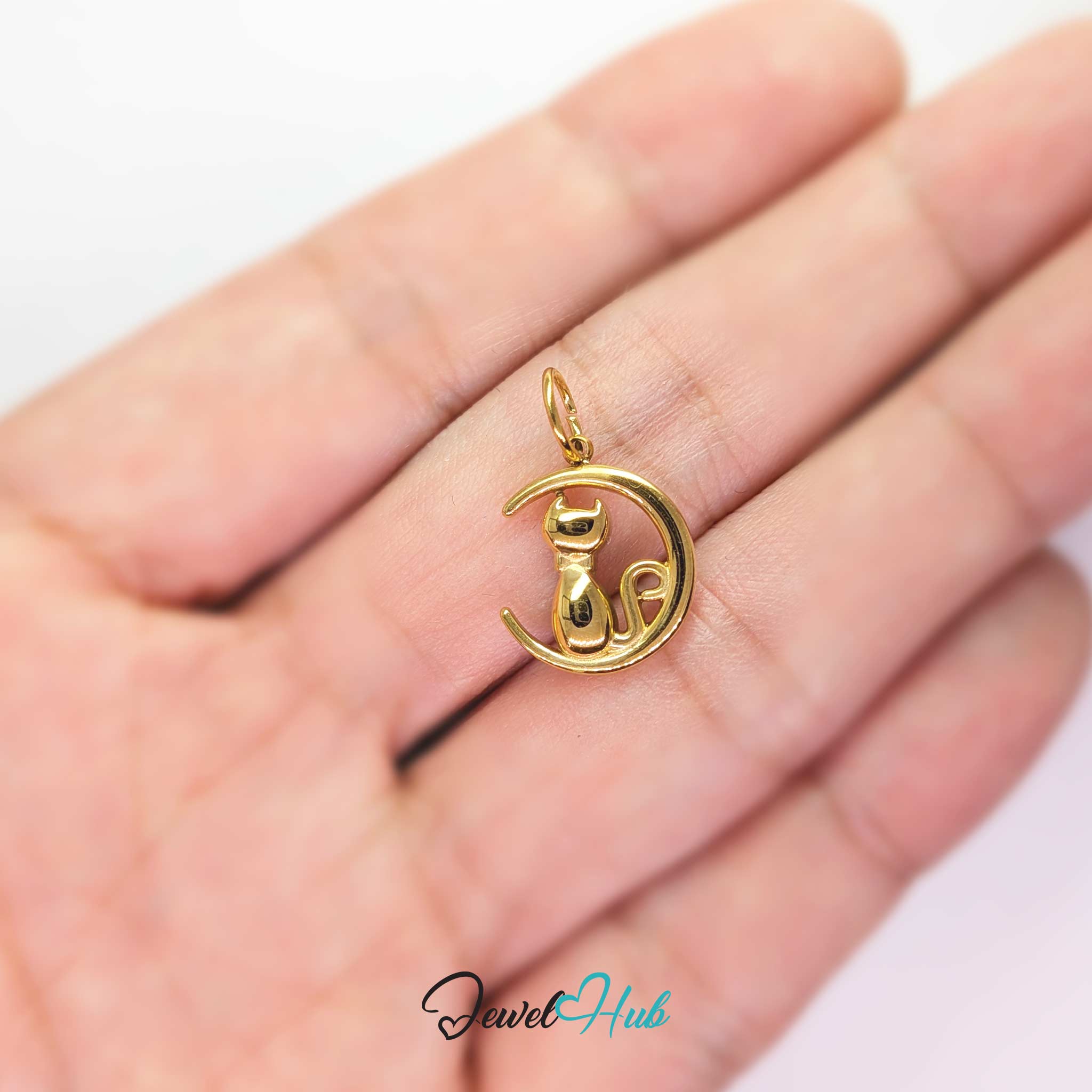 Gold cat and moon charm held in the hand to show its size against a fingertip - JewelHub
