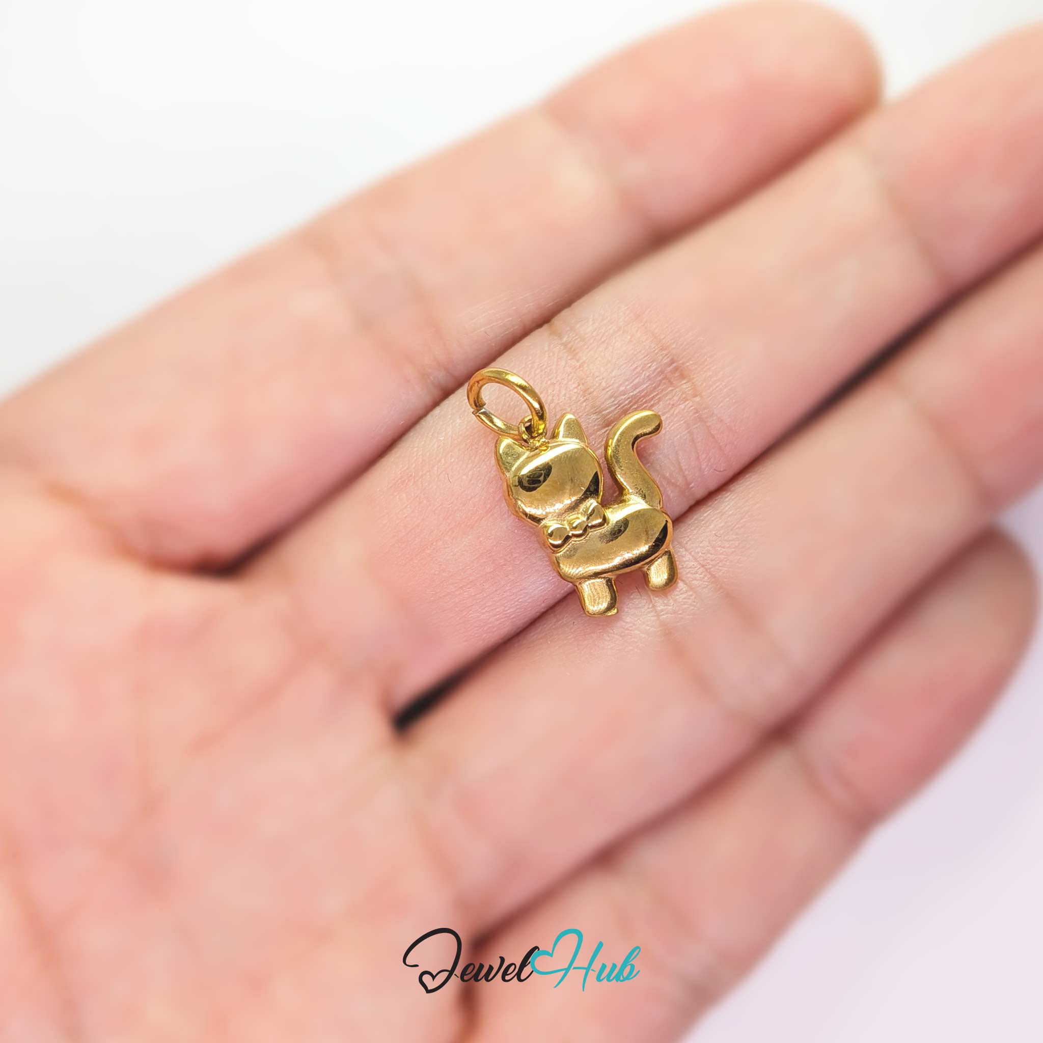 Gold cute cat charm held in the hand to show its size against a fingertip - JewelHub