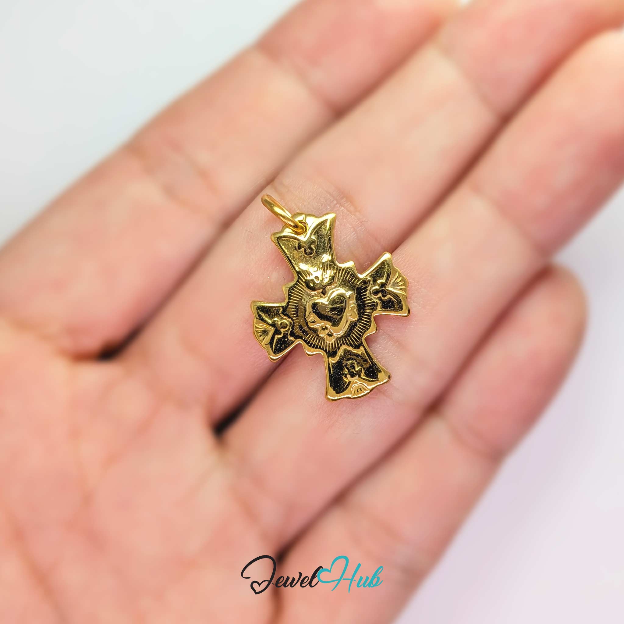 Dove cross charm in gold stainless steel with a radiant heart - held in the hand for scale - JewelHub