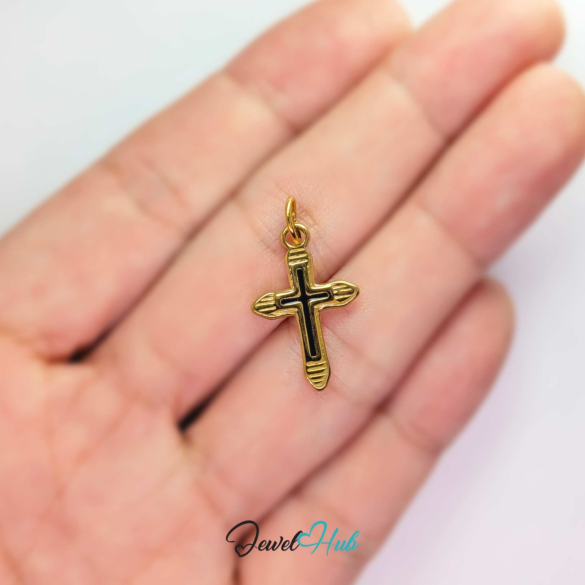 Cross charm in gold stainless steel with a black enamel inlay - held in the hand for scale - JewelHub