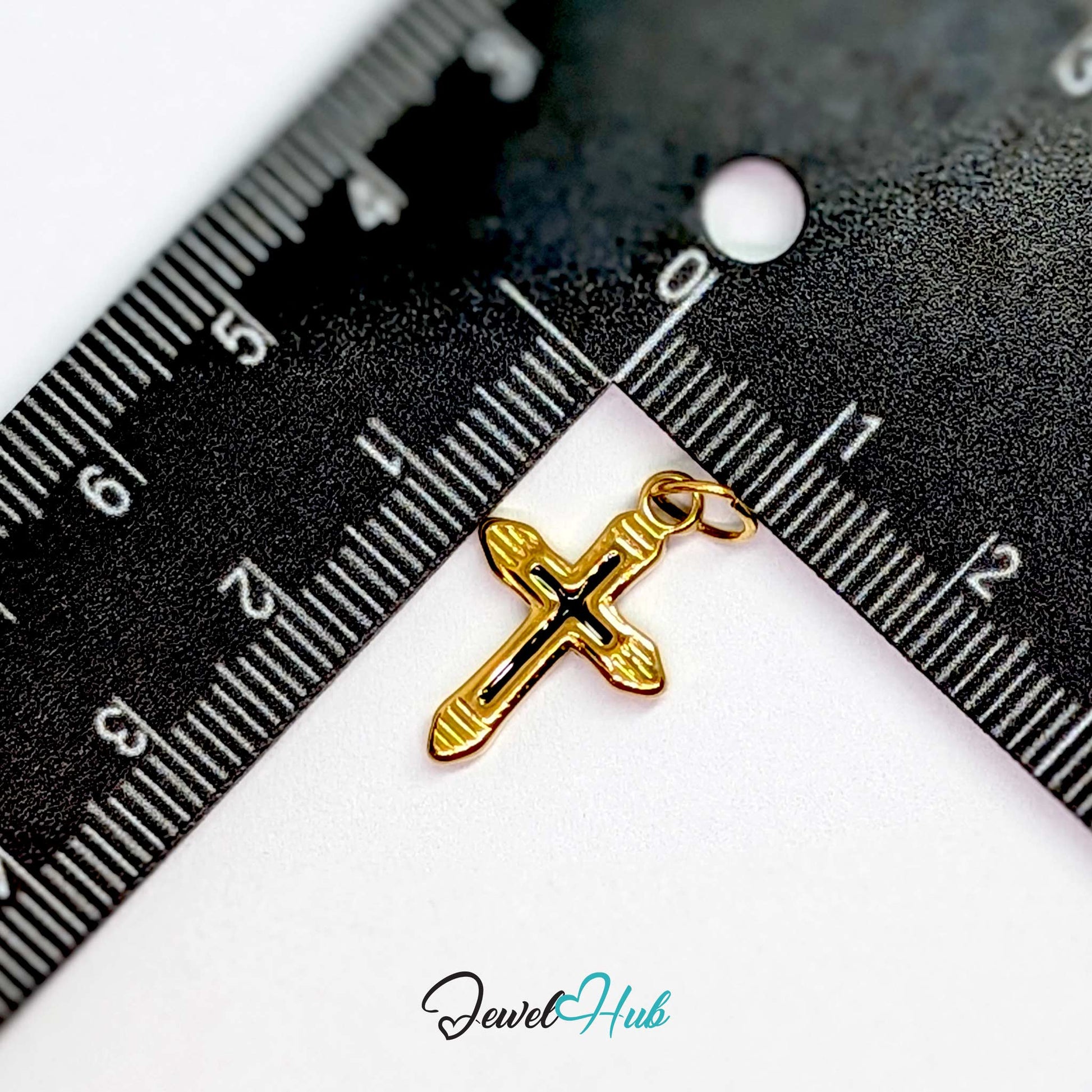 Cross charm in gold stainless steel with a black enamel inlay - beside a ruler for scale - JewelHub