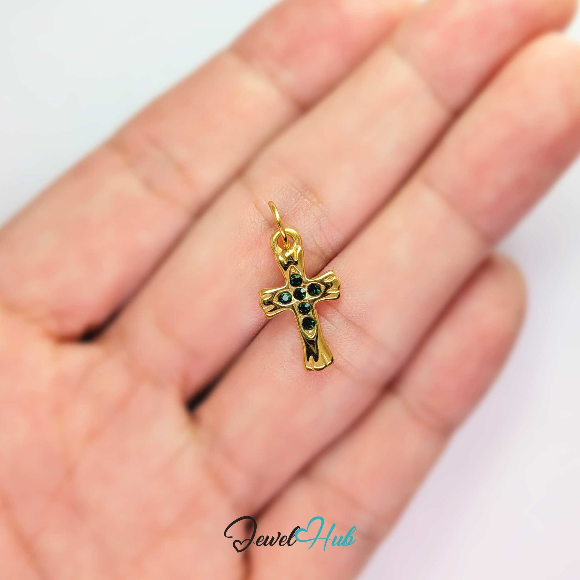Small cross charm in gold stainless steel with six green stones - held in the hand for scale - JewelHub