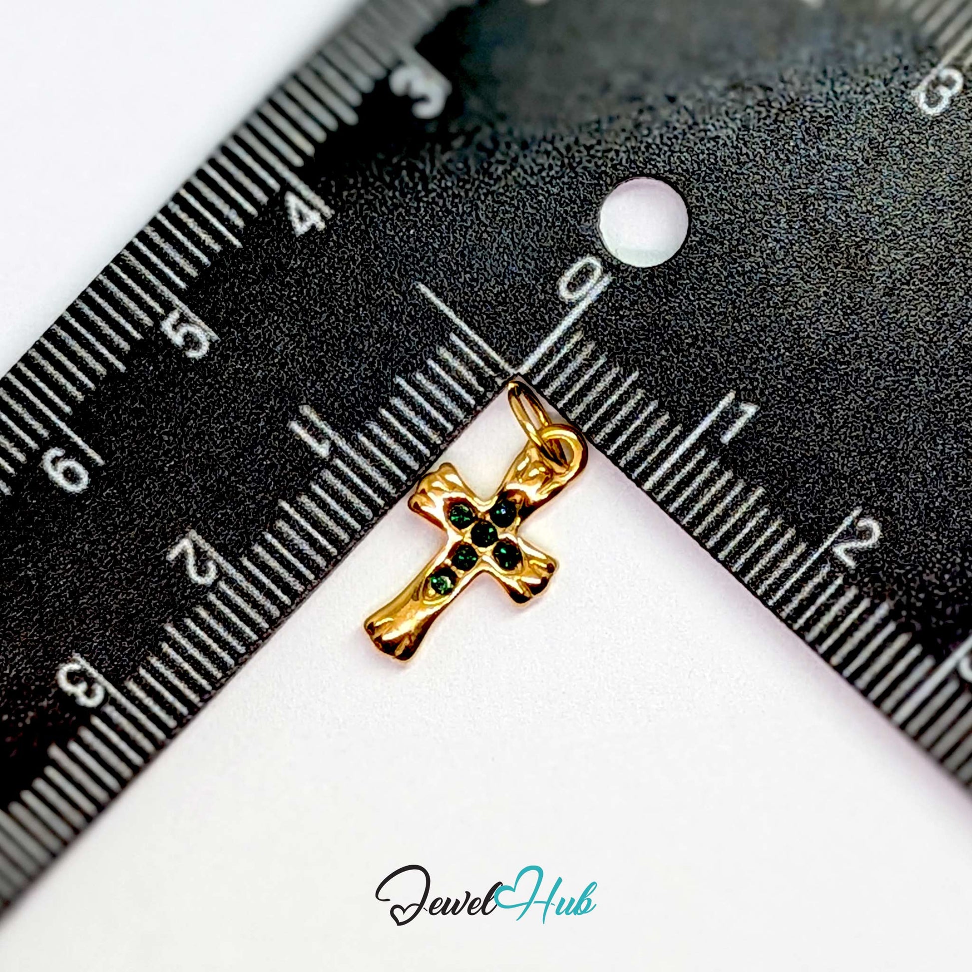 Small cross charm in gold stainless steel with six green stones - beside a ruler for scale - JewelHub