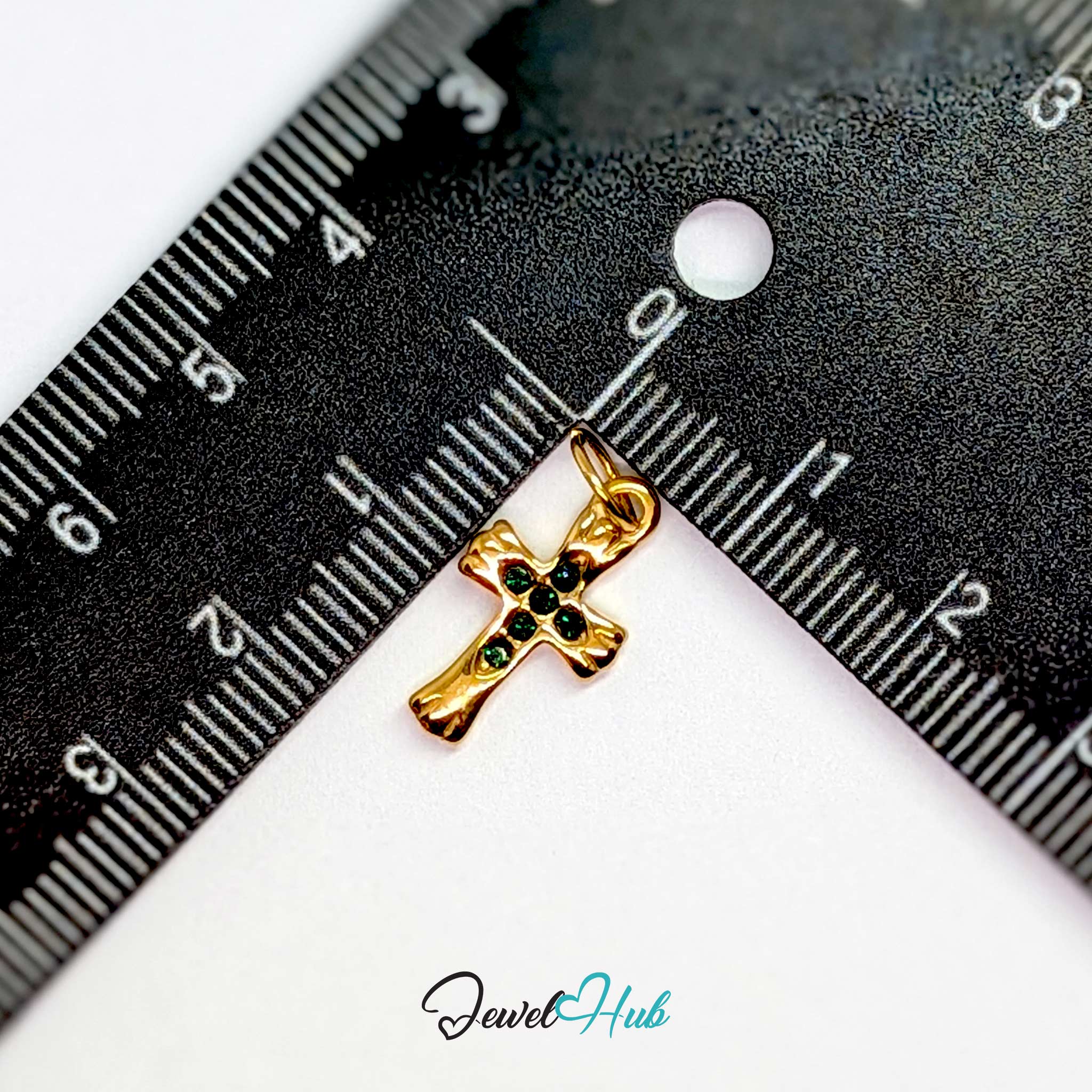 Small cross charm in gold stainless steel with six green stones - beside a ruler for scale - JewelHub