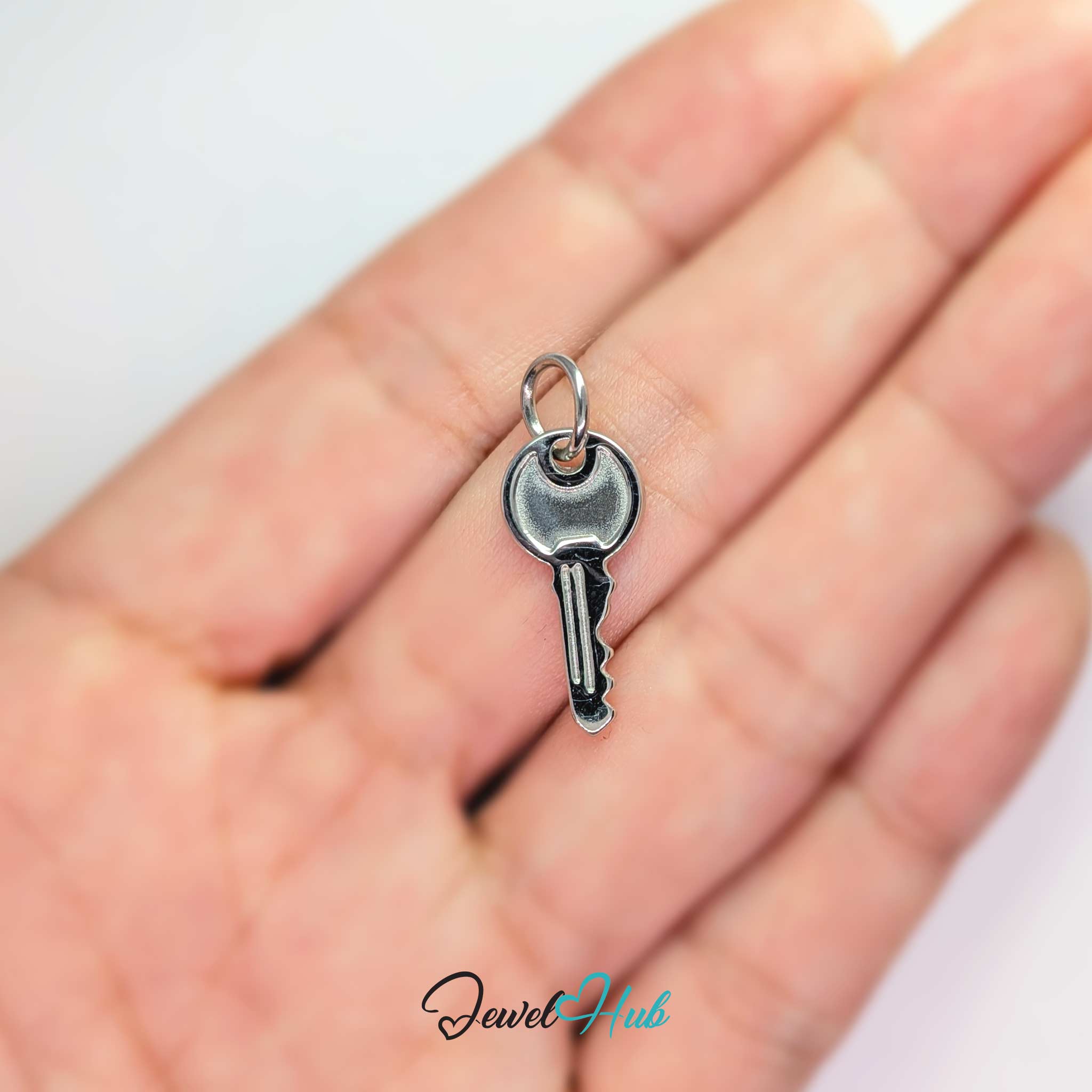 Everyday key charm in silver stainless steel with a plain round head - held in the hand for scale - JewelHub