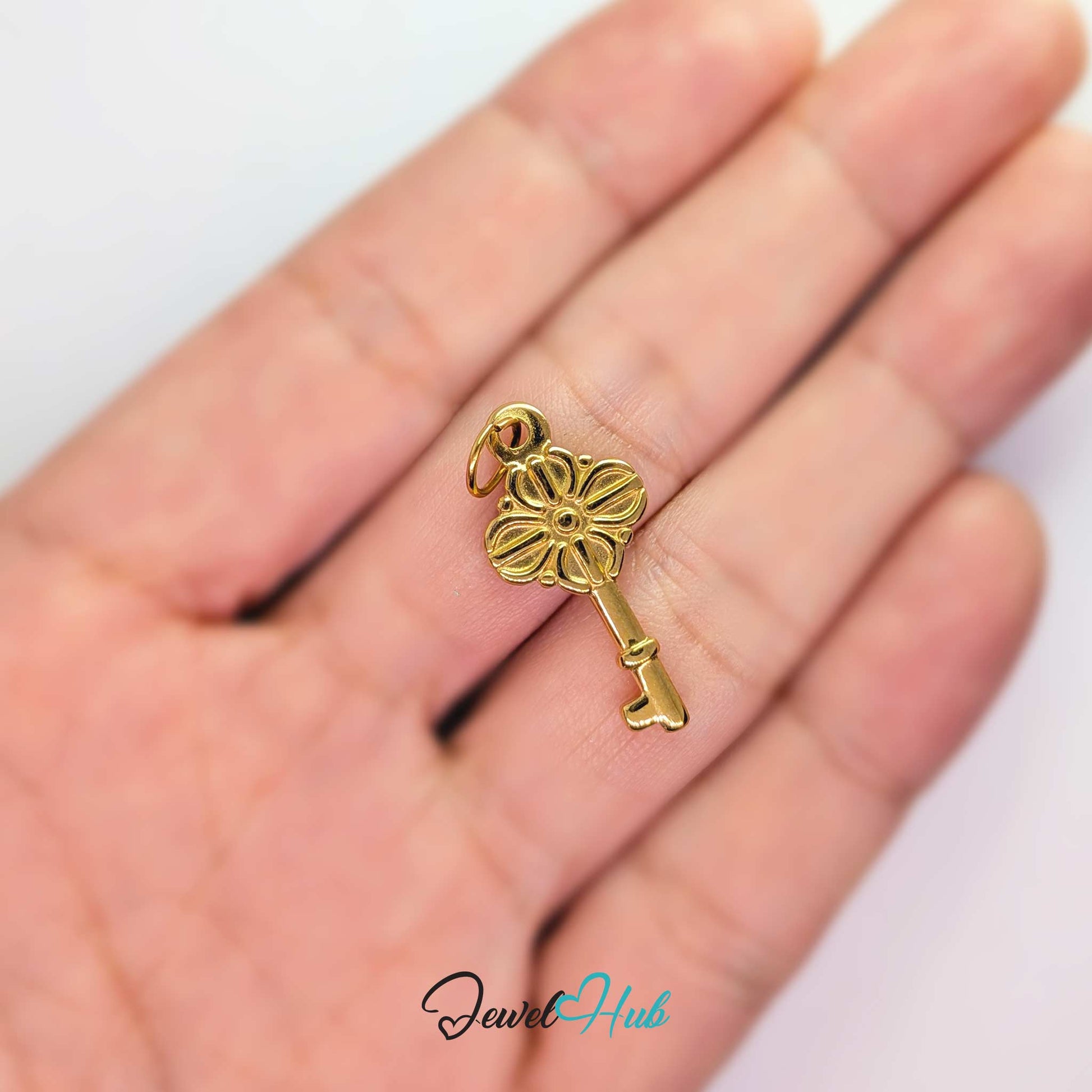 Vintage key charm in gold stainless steel with a quatrefoil bow - held in the hand for scale - JewelHub