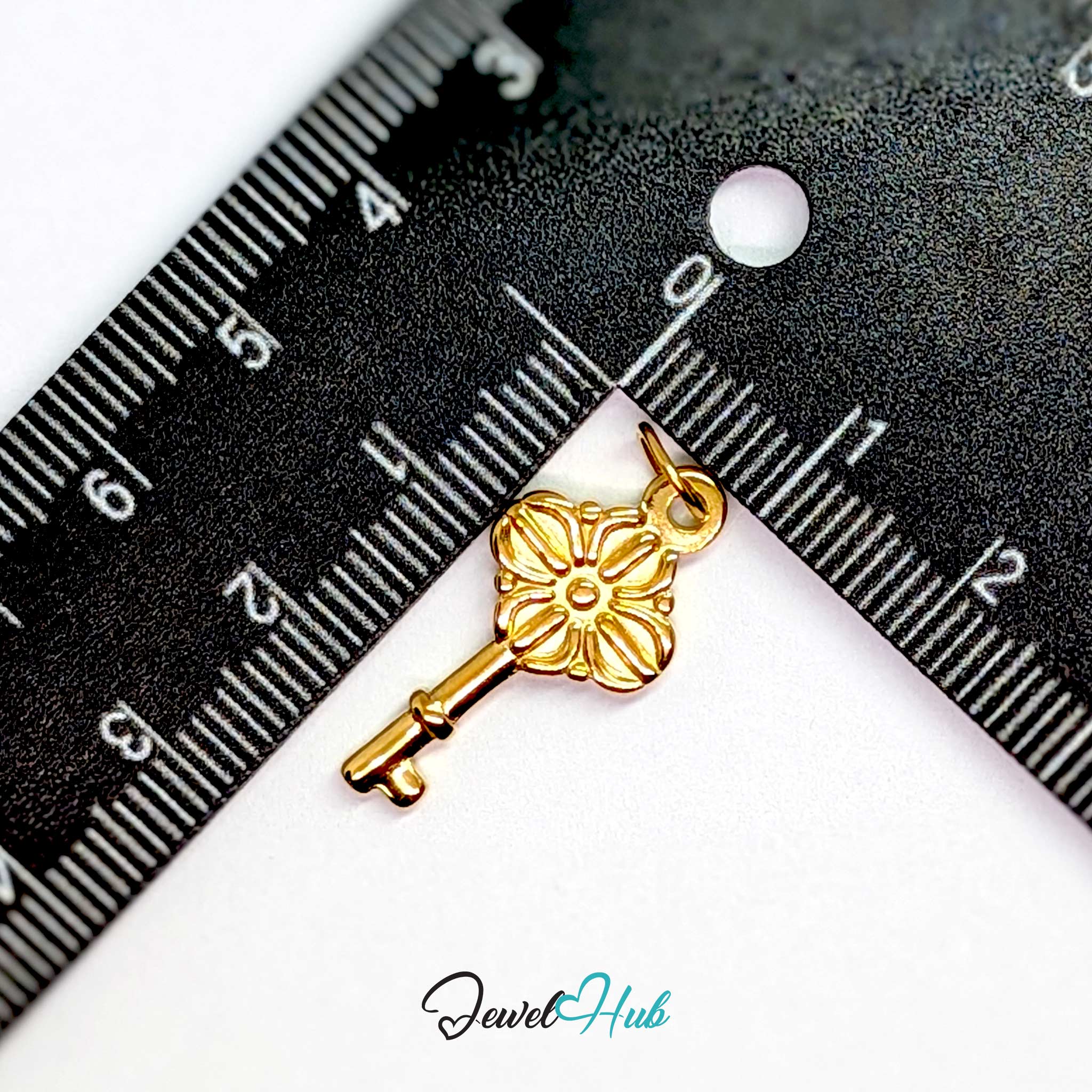 Vintage key charm in gold stainless steel with a quatrefoil bow - beside a ruler for scale - JewelHub
