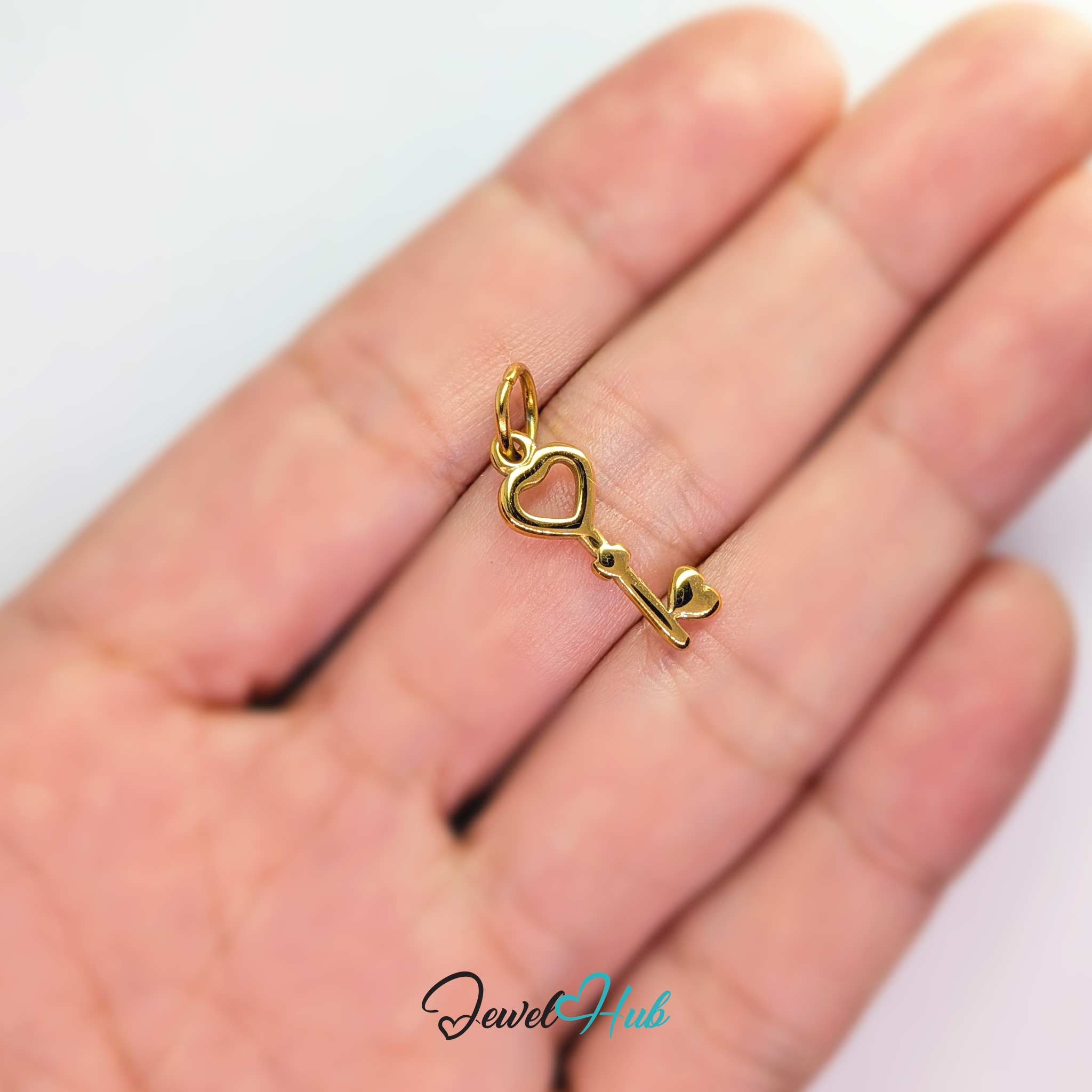 Heart key charm in gold stainless steel with an open heart bow - held in the hand for scale - JewelHub