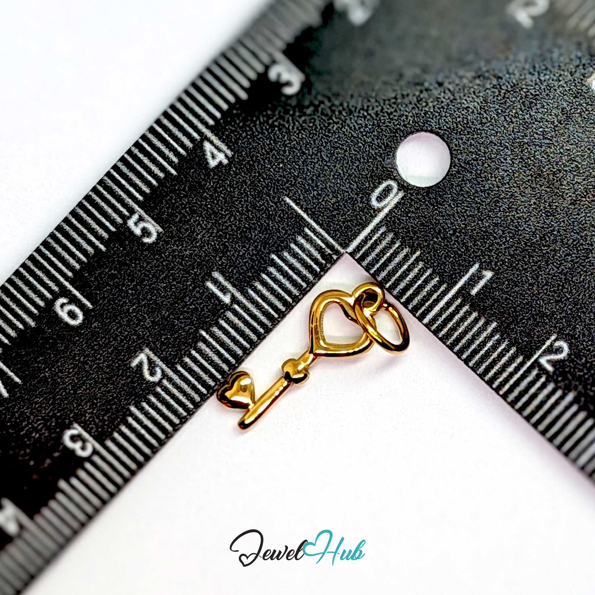 Heart key charm in gold stainless steel with an open heart bow - beside a ruler for scale - JewelHub