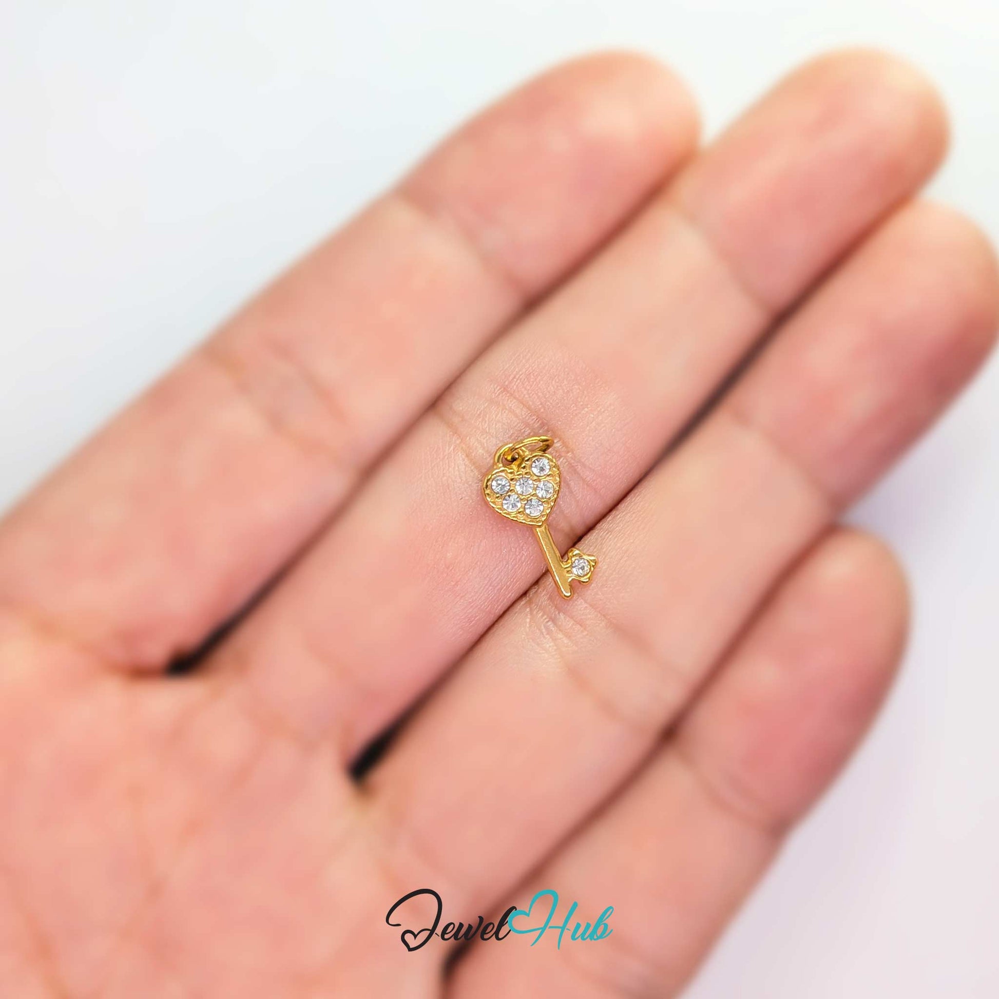 Mini heart key charm in gold stainless steel set with crystals - held in the hand for scale - JewelHub