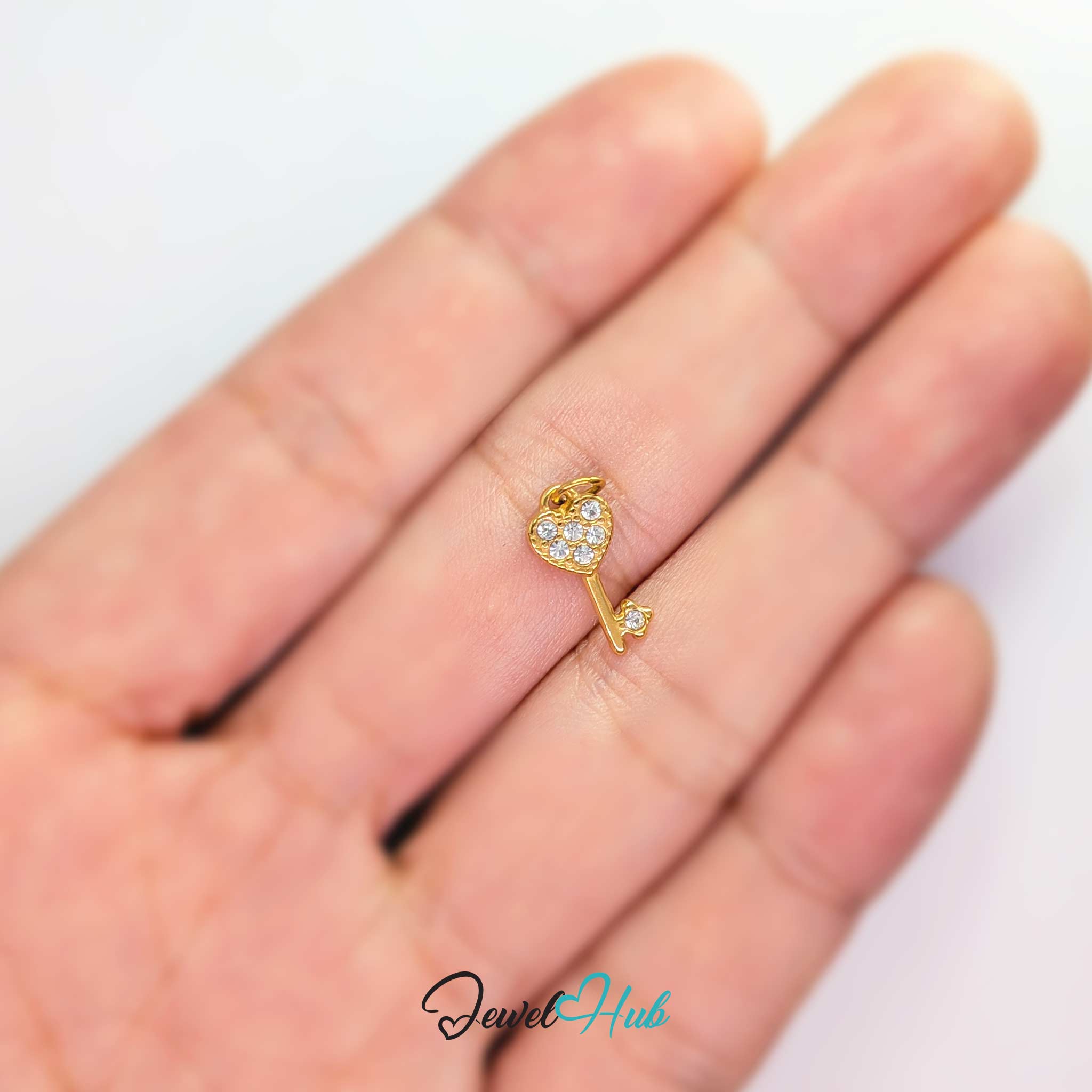 Mini heart key charm in gold stainless steel set with crystals - held in the hand for scale - JewelHub