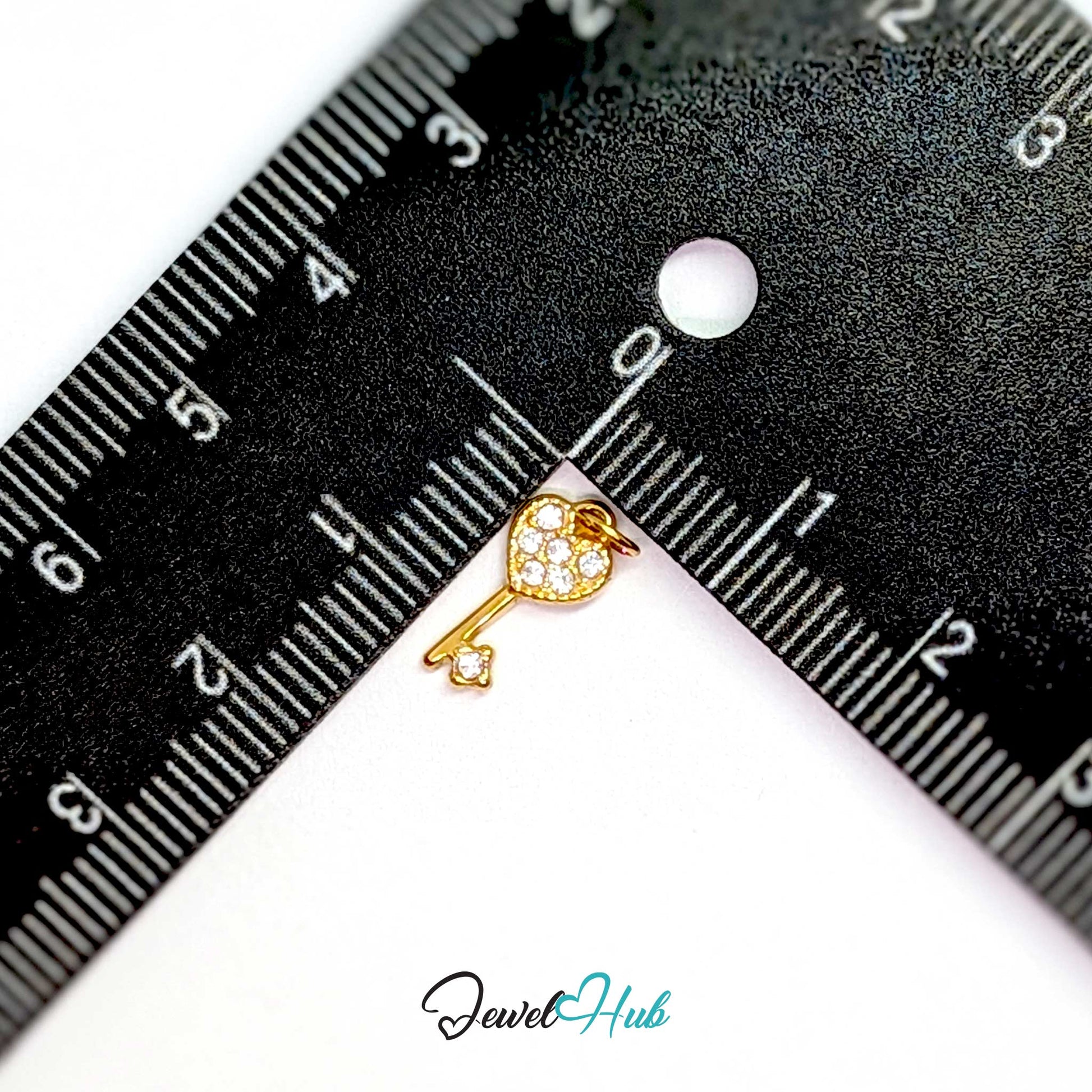 Mini heart key charm in gold stainless steel set with crystals - beside a ruler for scale - JewelHub