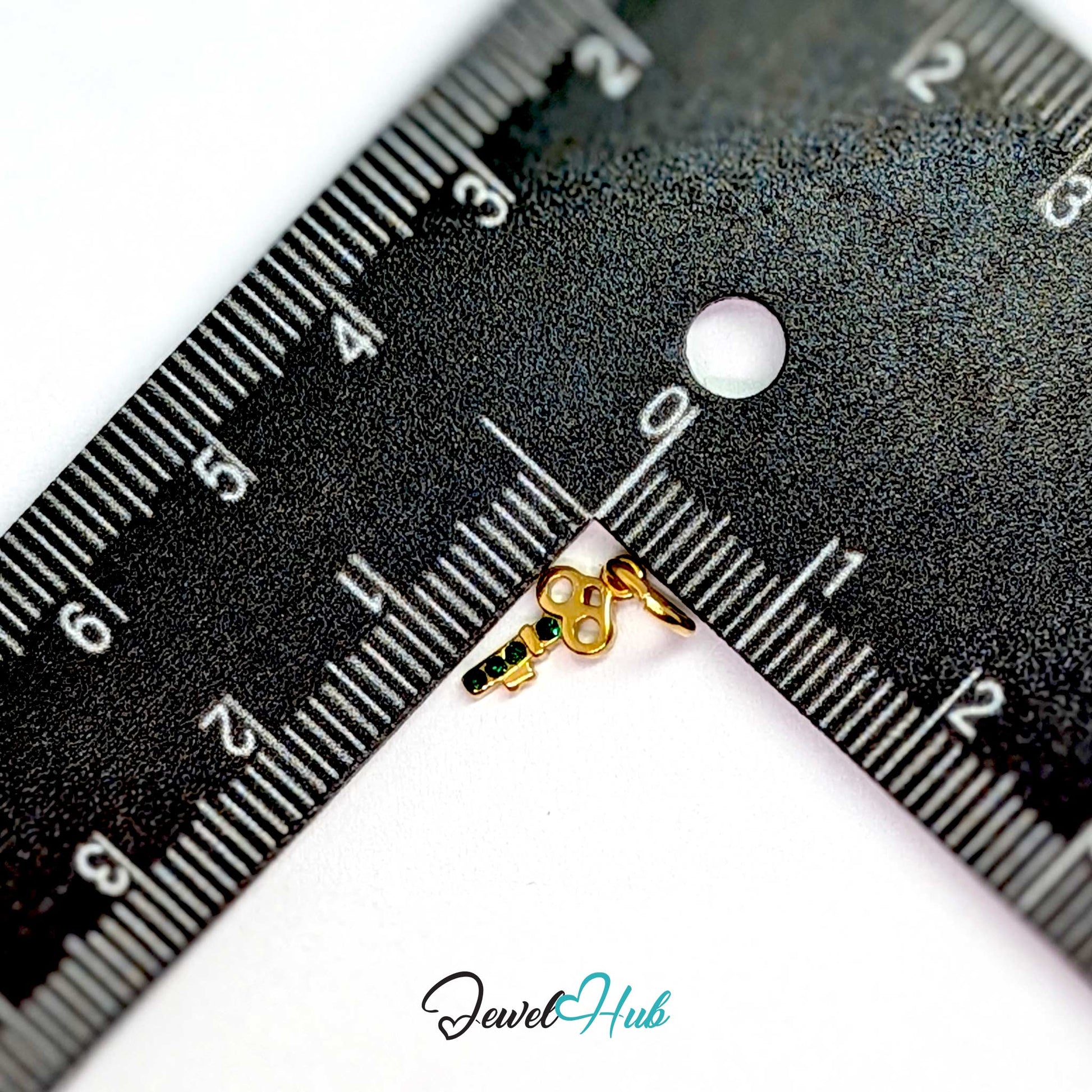 Mini key charm in gold stainless steel with four green stones - beside a ruler for scale - JewelHub