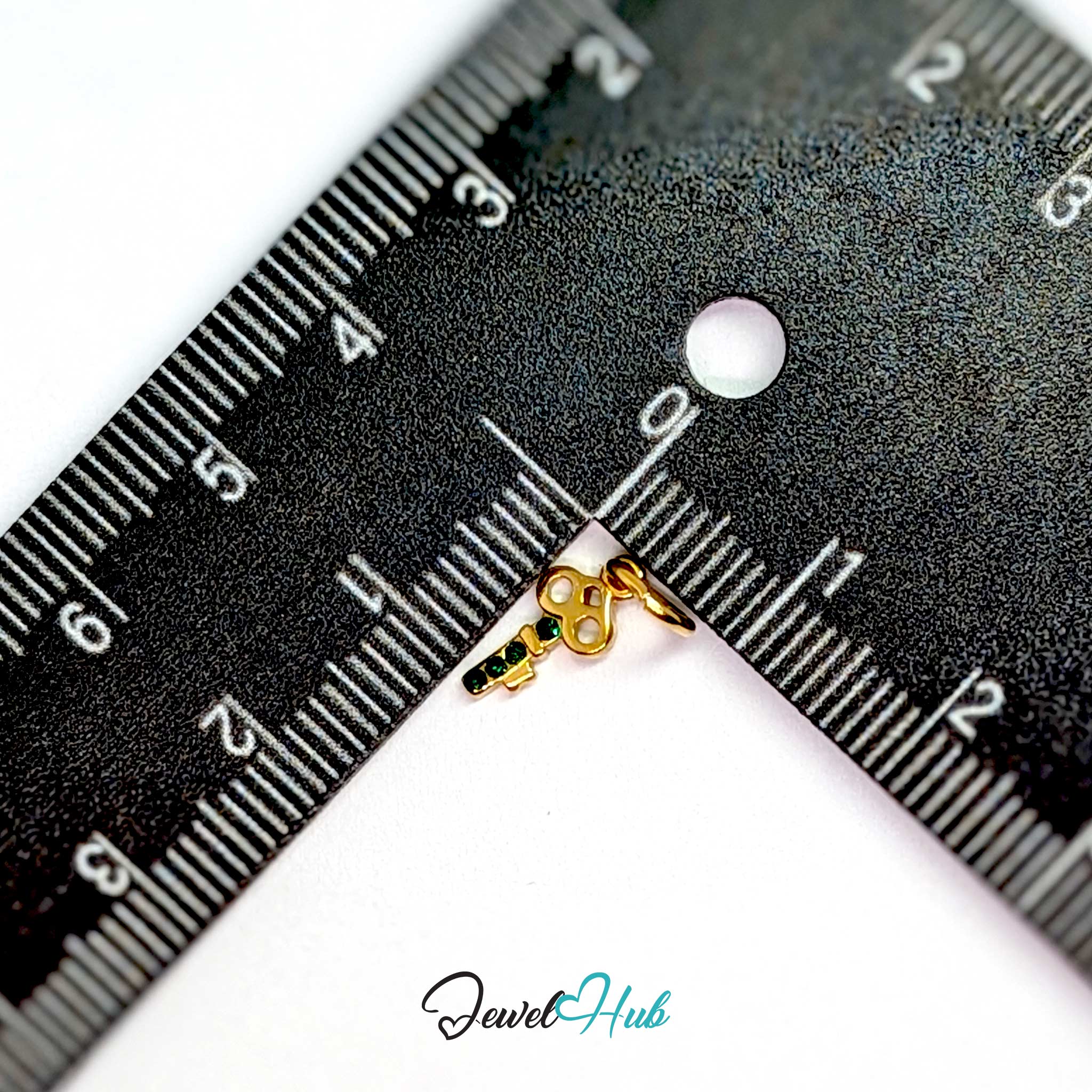 Mini key charm in gold stainless steel with four green stones - beside a ruler for scale - JewelHub