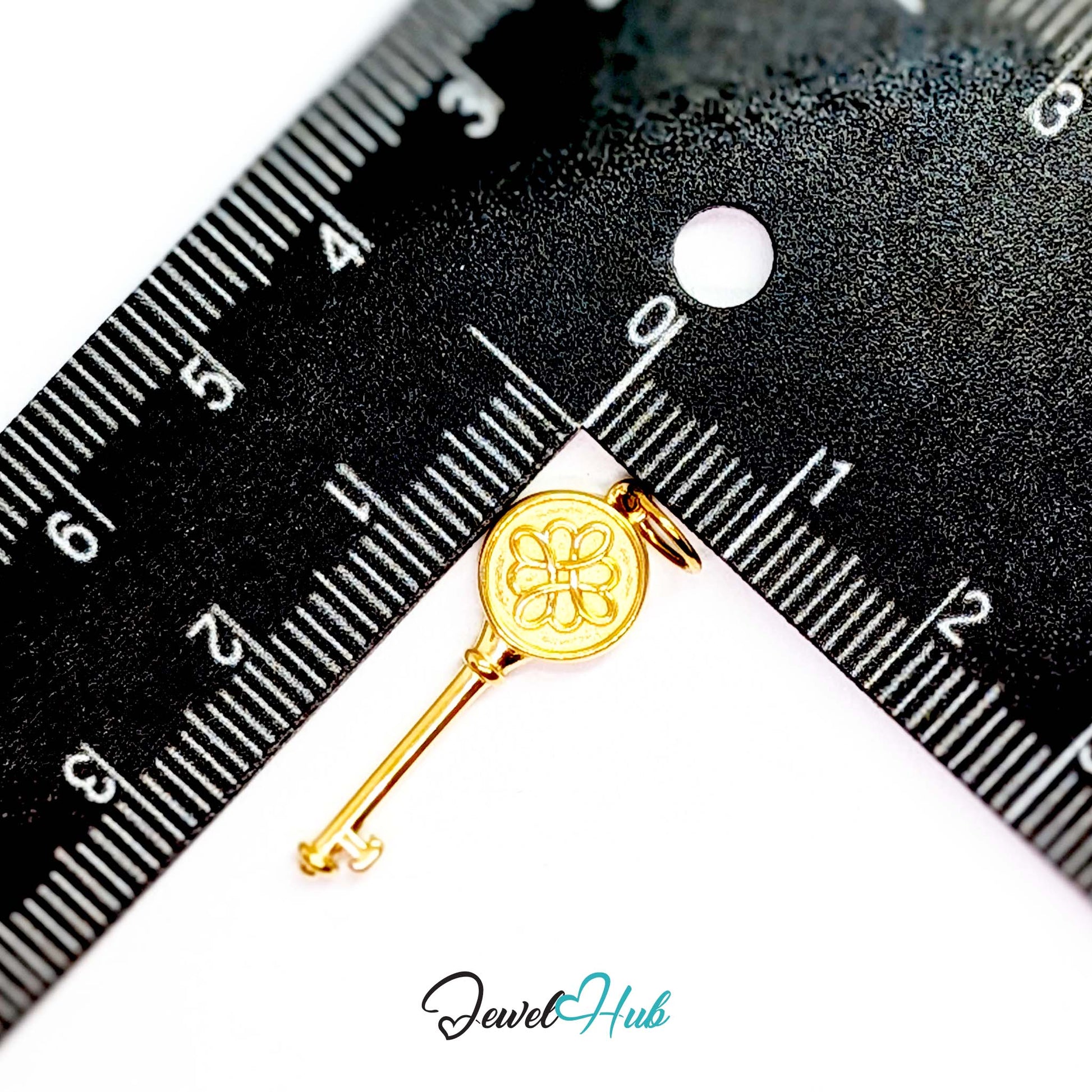 Round openwork key charm in gold stainless steel - beside a ruler for scale - JewelHub