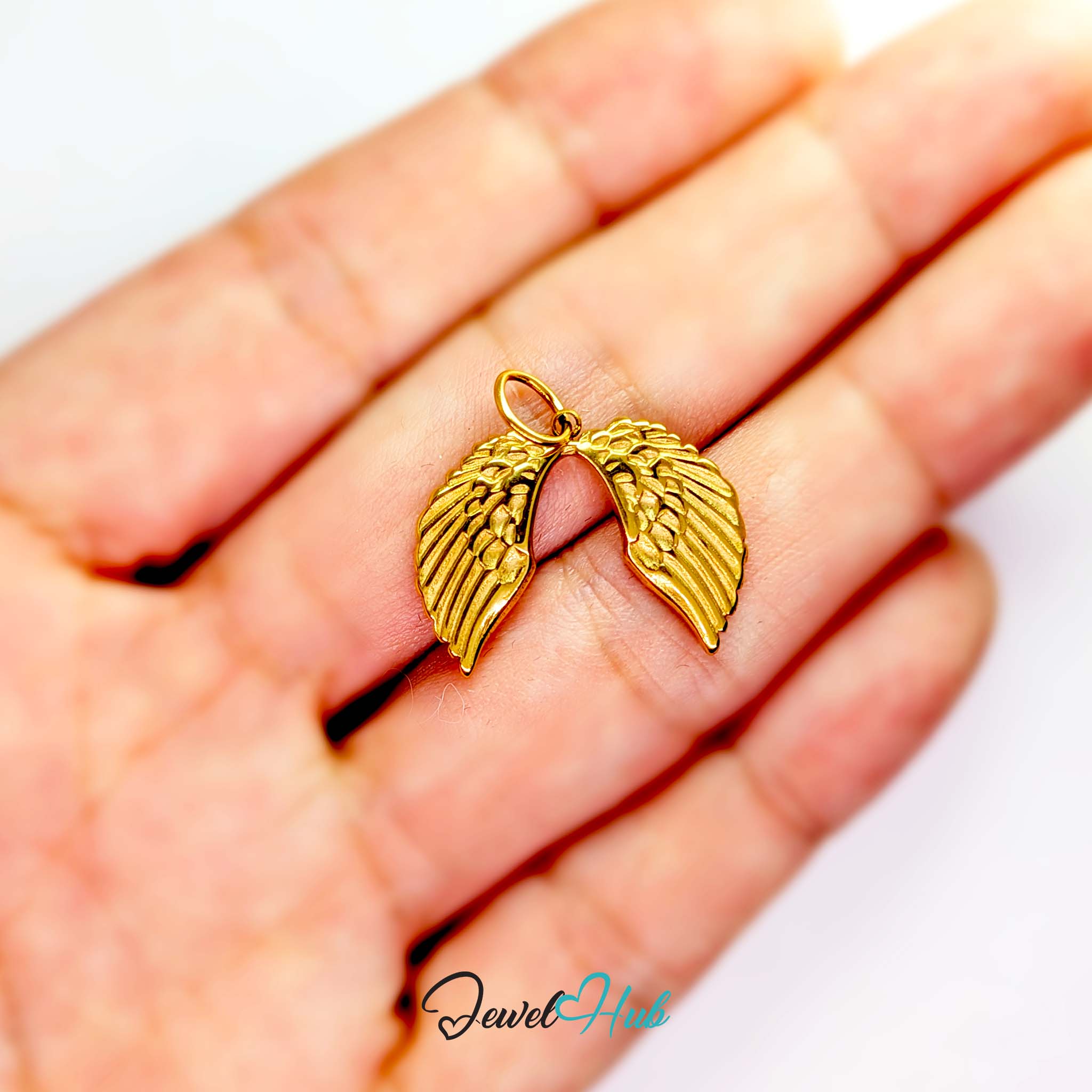 Angel wings charm in gold stainless steel - held in the hand for scale - JewelHub