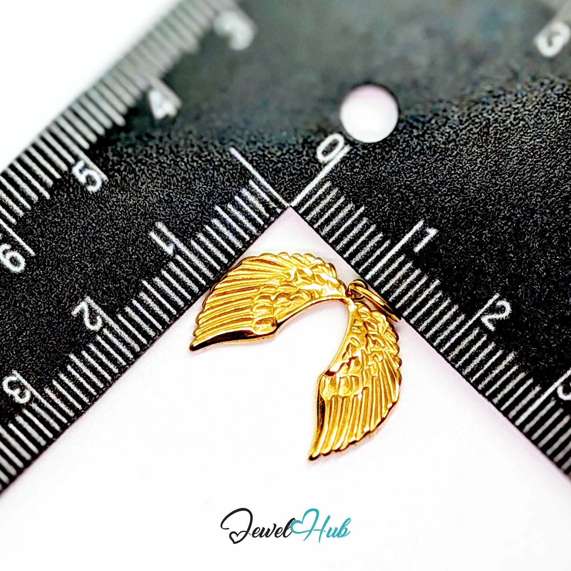 Angel wings charm in gold stainless steel - beside a ruler for scale - JewelHub