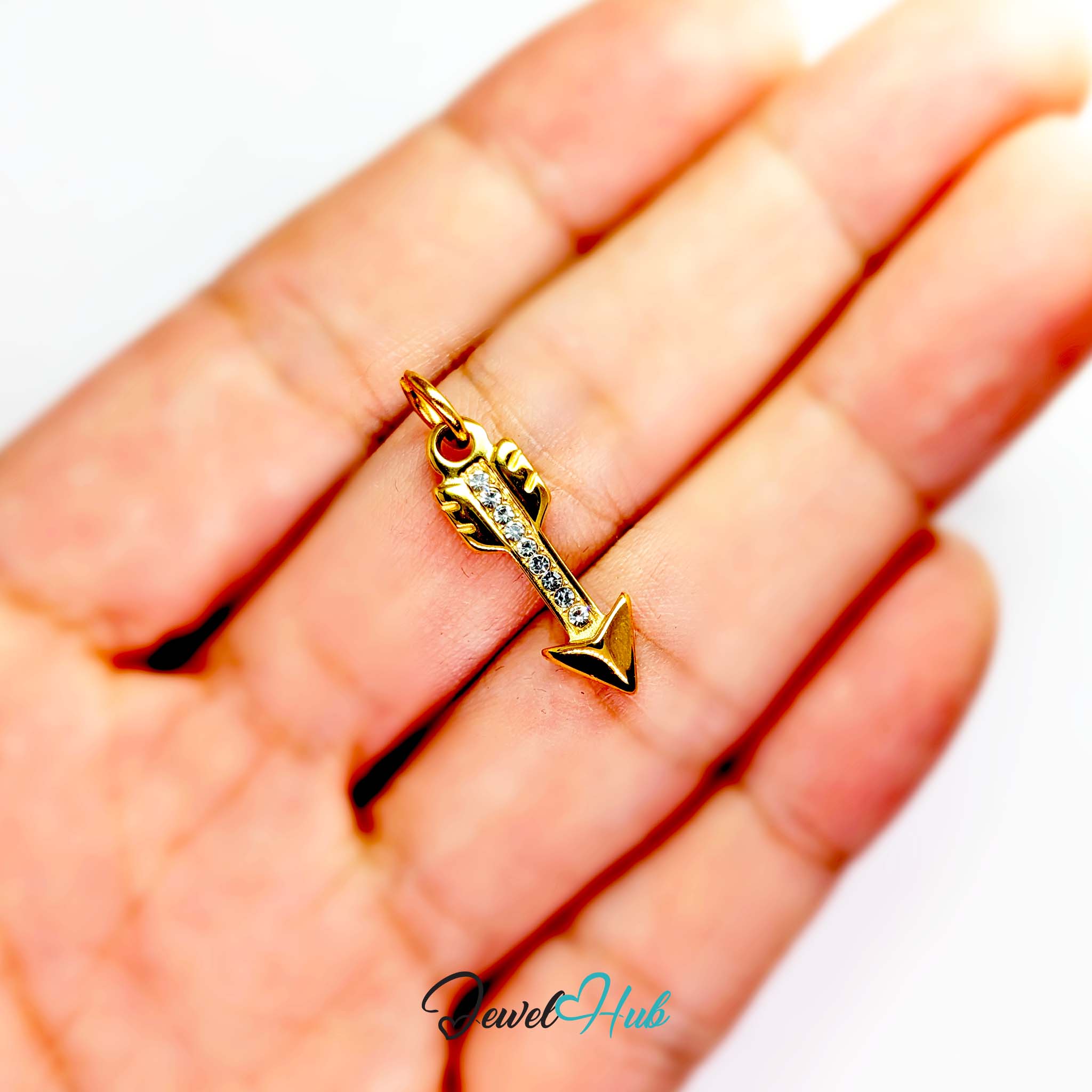 Arrow charm in gold stainless steel with clear crystals - held in the hand for scale - JewelHub