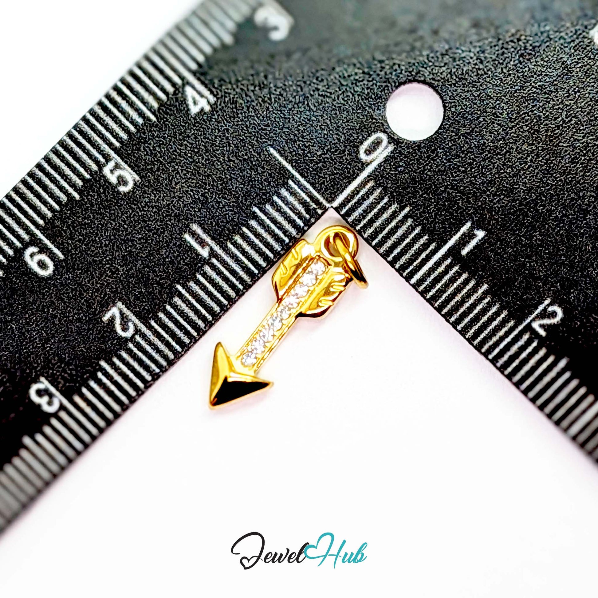 Arrow charm in gold stainless steel with clear crystals - beside a ruler for scale - JewelHub