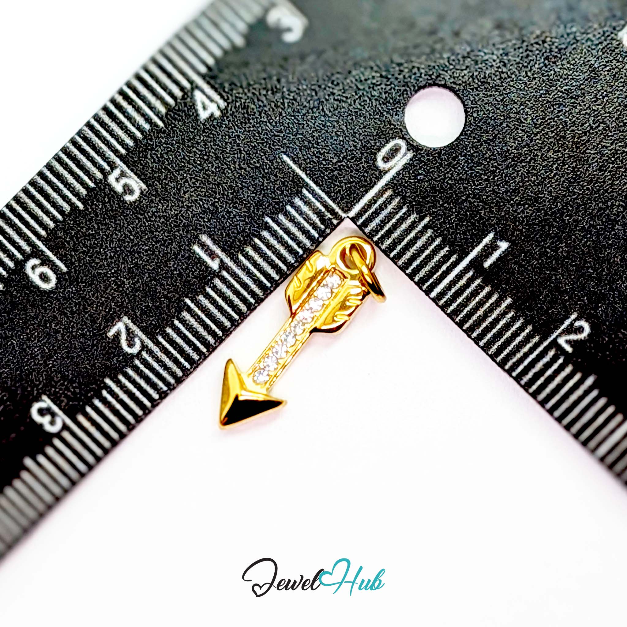 Arrow charm in gold stainless steel with clear crystals - beside a ruler for scale - JewelHub