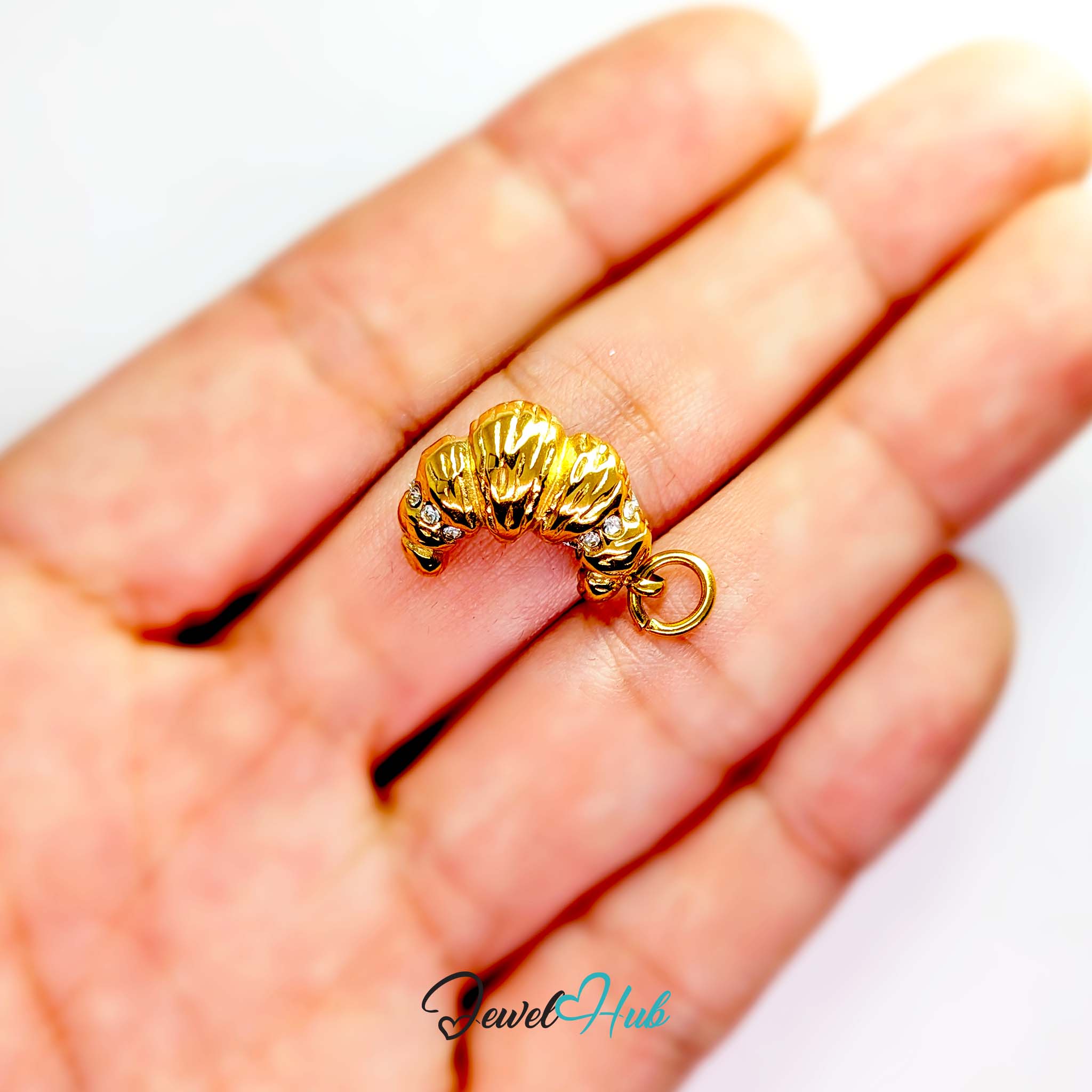 Croissant charm in gold stainless steel with clear crystals - held in the hand for scale - JewelHub