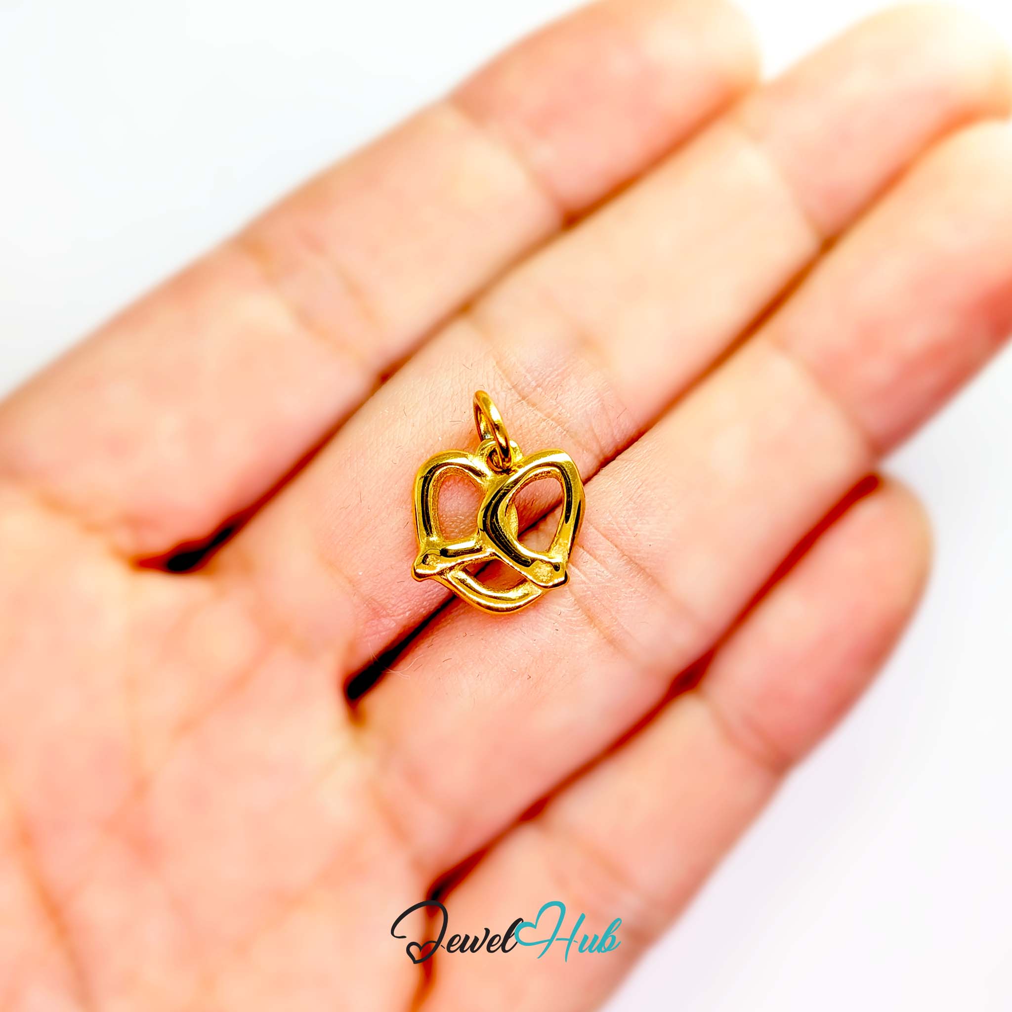 Openwork pretzel charm in gold stainless steel - held in the hand for scale - JewelHub