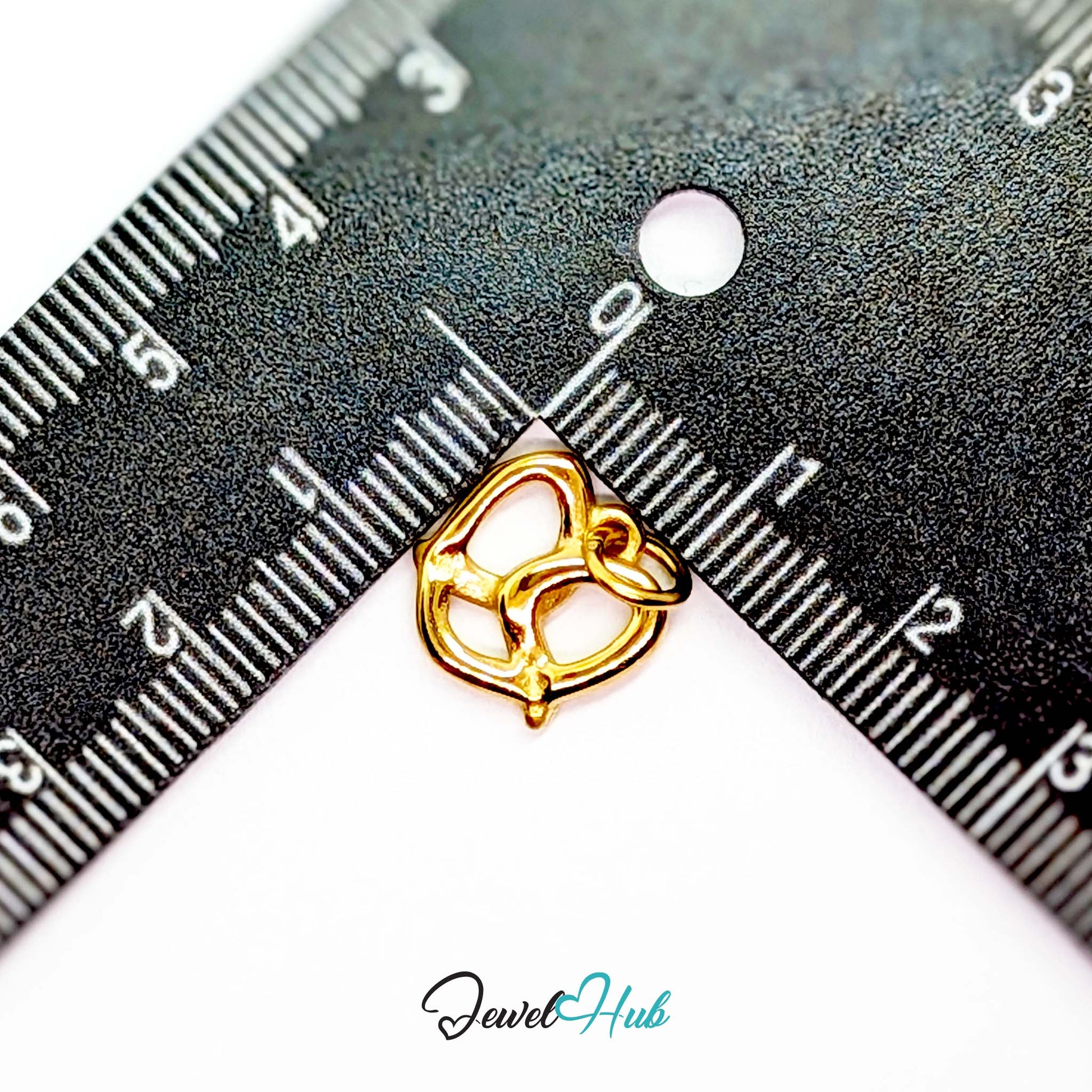 Openwork pretzel charm in gold stainless steel - beside a ruler for scale - JewelHub