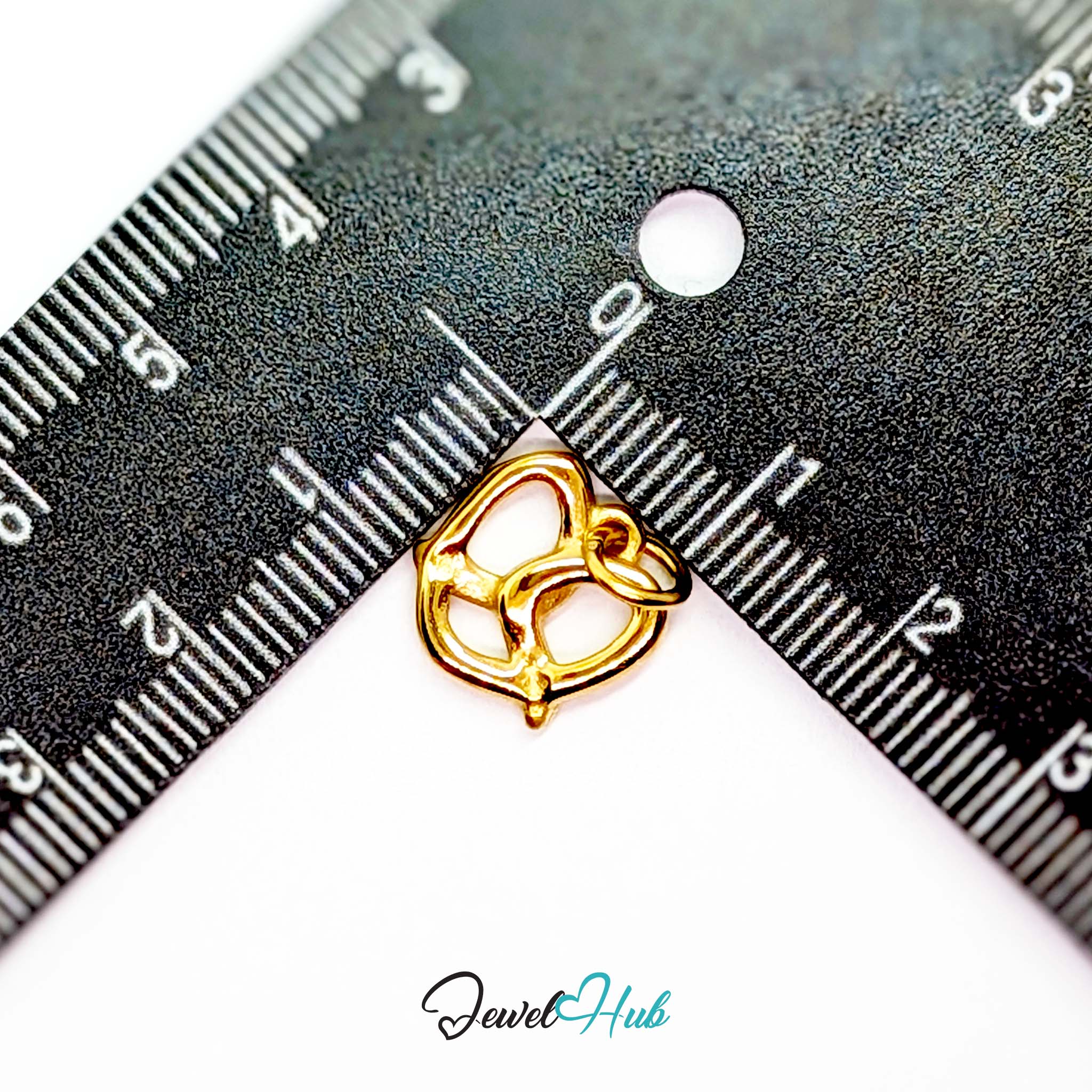 Openwork pretzel charm in gold stainless steel - beside a ruler for scale - JewelHub