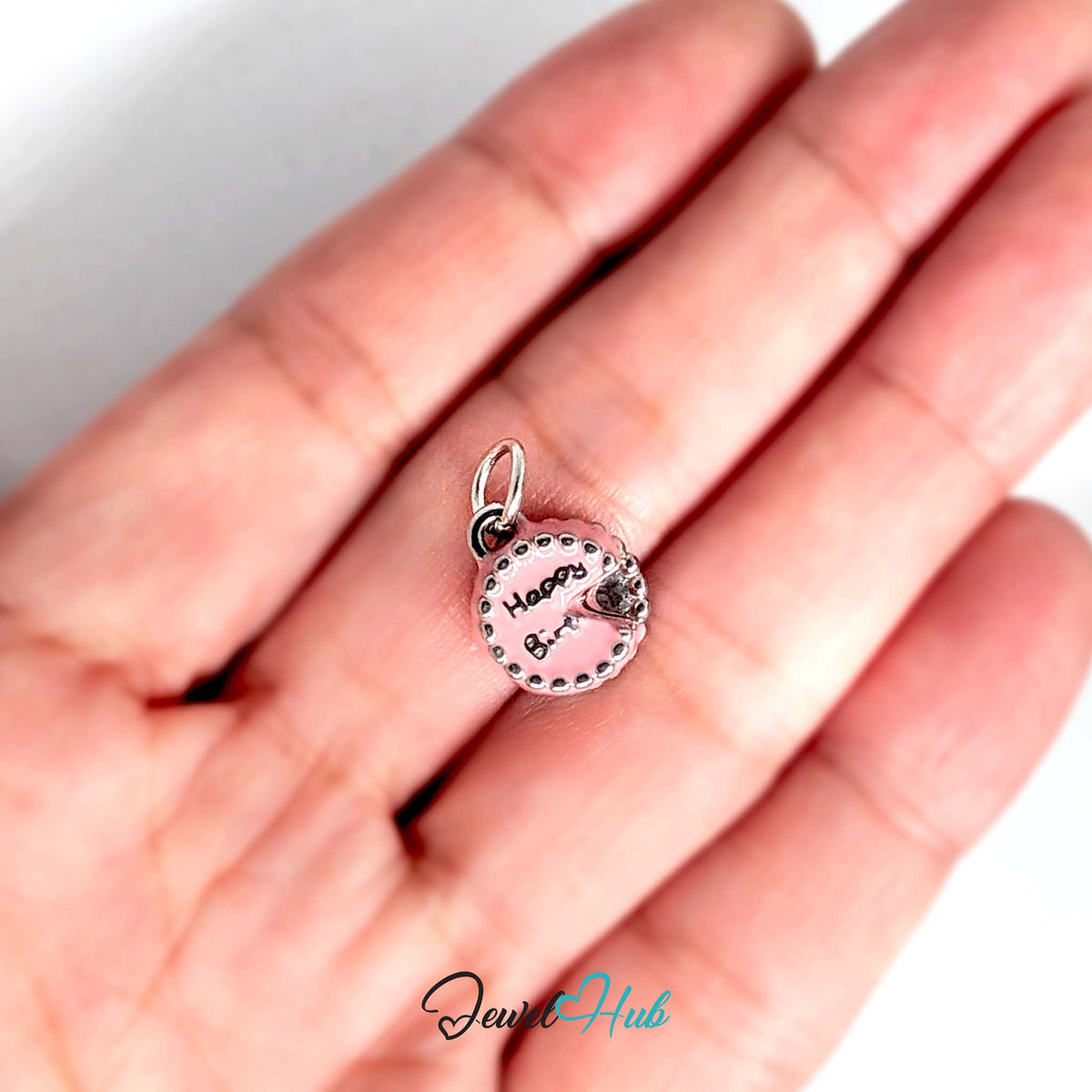 Pink birthday cake charm held in a hand to show its size - JewelHub
