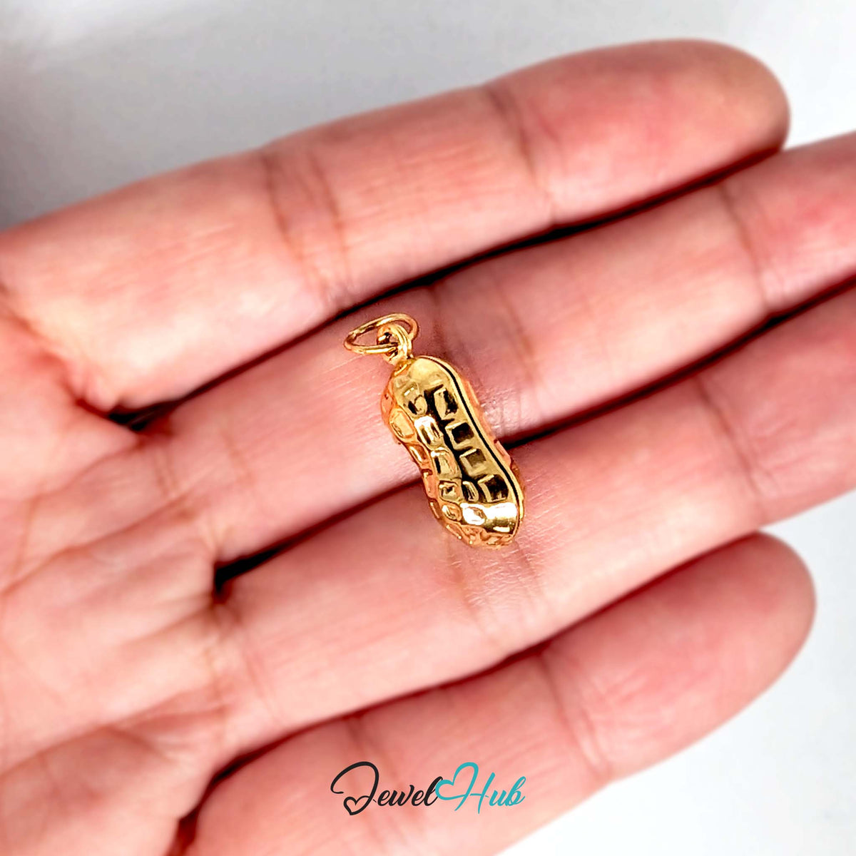 Hammered peanut charm held in a hand to show its size - JewelHub