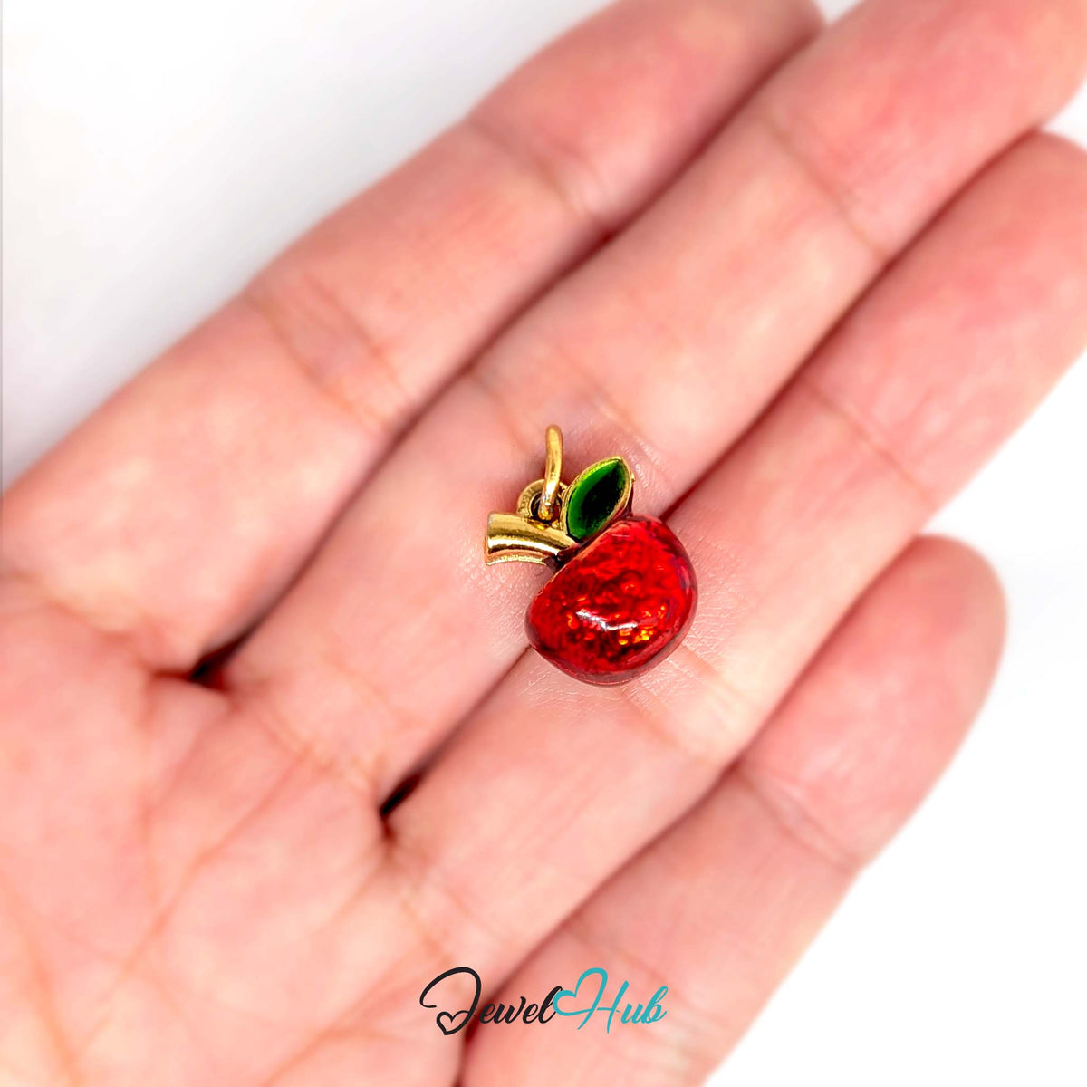 Red apple charm held in a hand to show its size - JewelHub