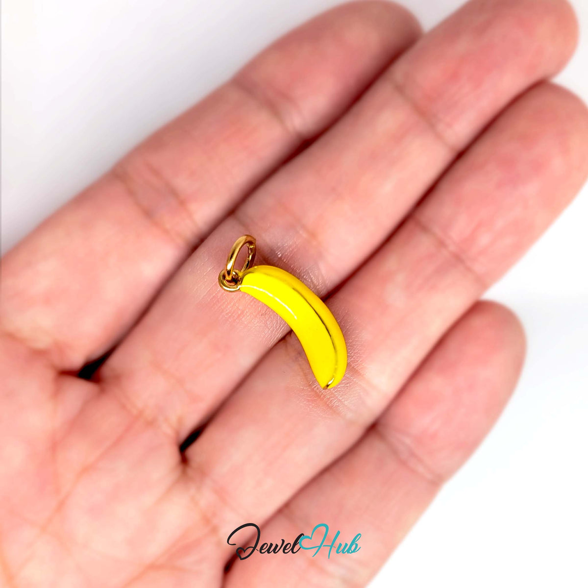 Yellow enamel banana charm held in a hand to show its size - JewelHub