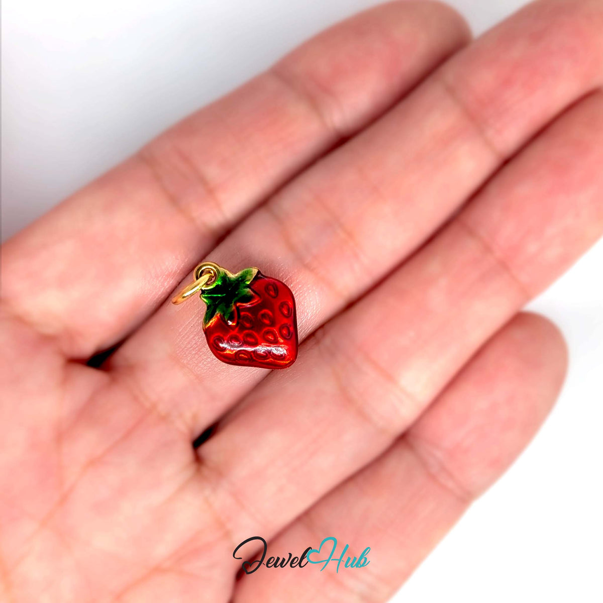 Red enamel strawberry charm held in a hand to show its size - JewelHub