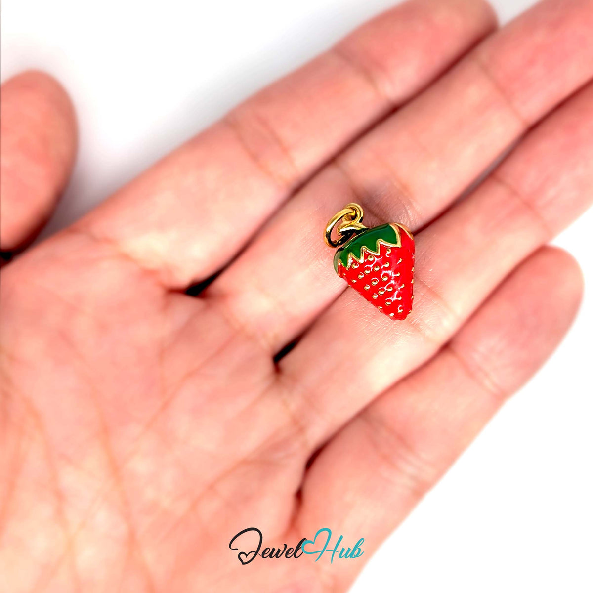3D red enamel strawberry charm held in a hand to show its size - JewelHub