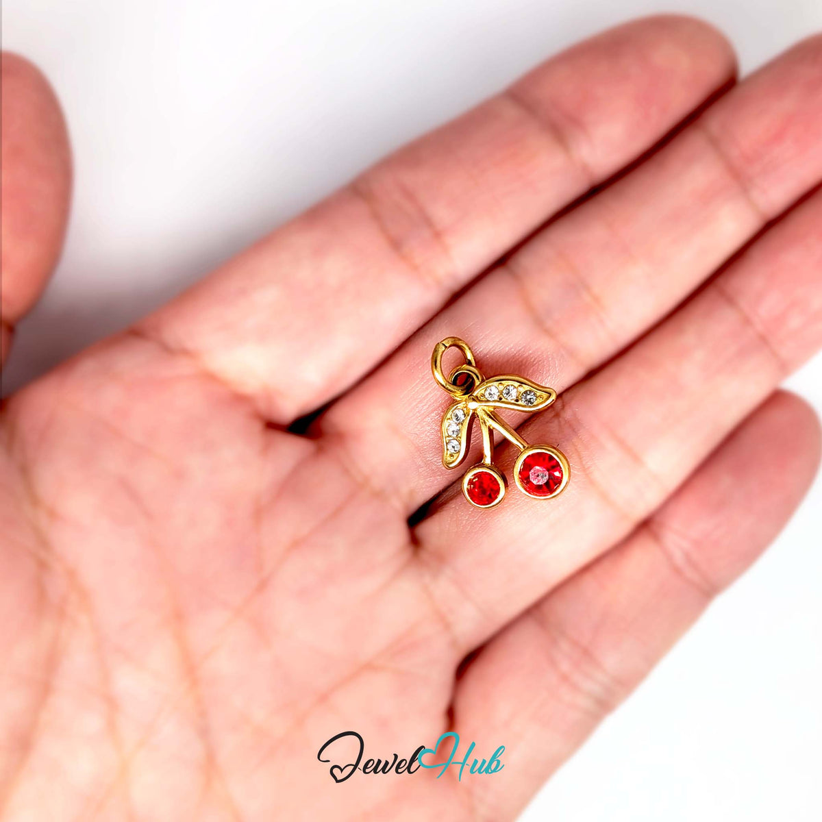 Red gem cherry charm held in a hand to show its size - JewelHub