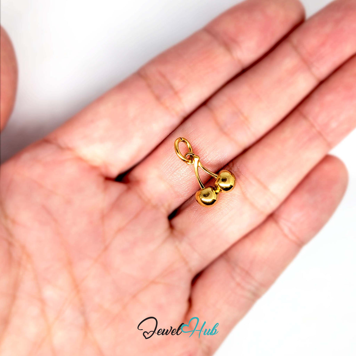 Polished cherry charm held in a hand to show its size - JewelHub