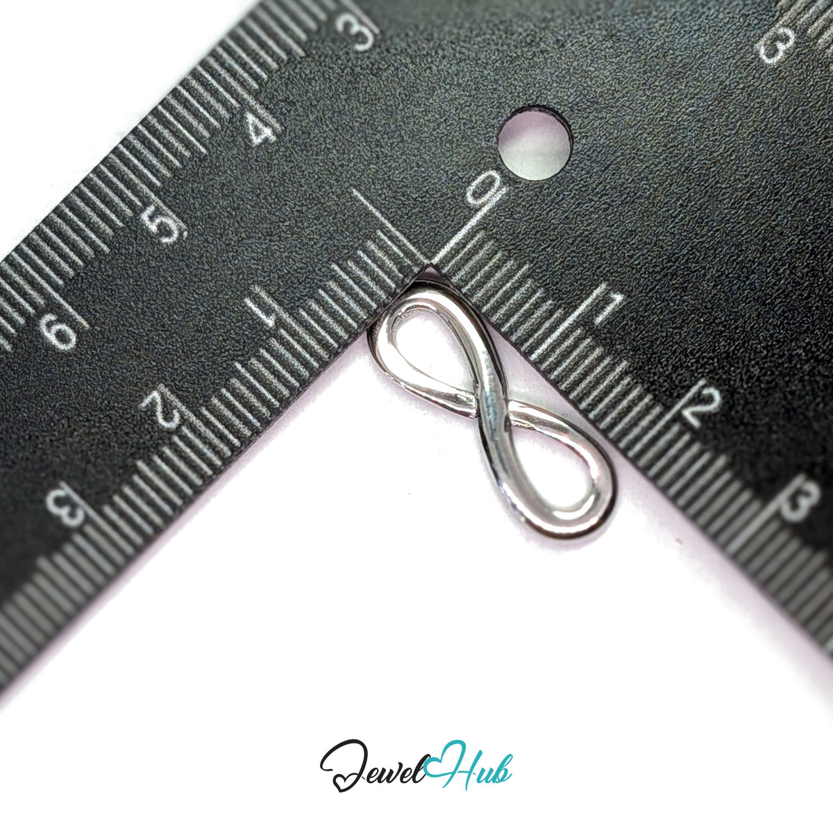 Infinity charm measured against a ruler at 8.2mm wide by 23.8mm tall - JewelHub