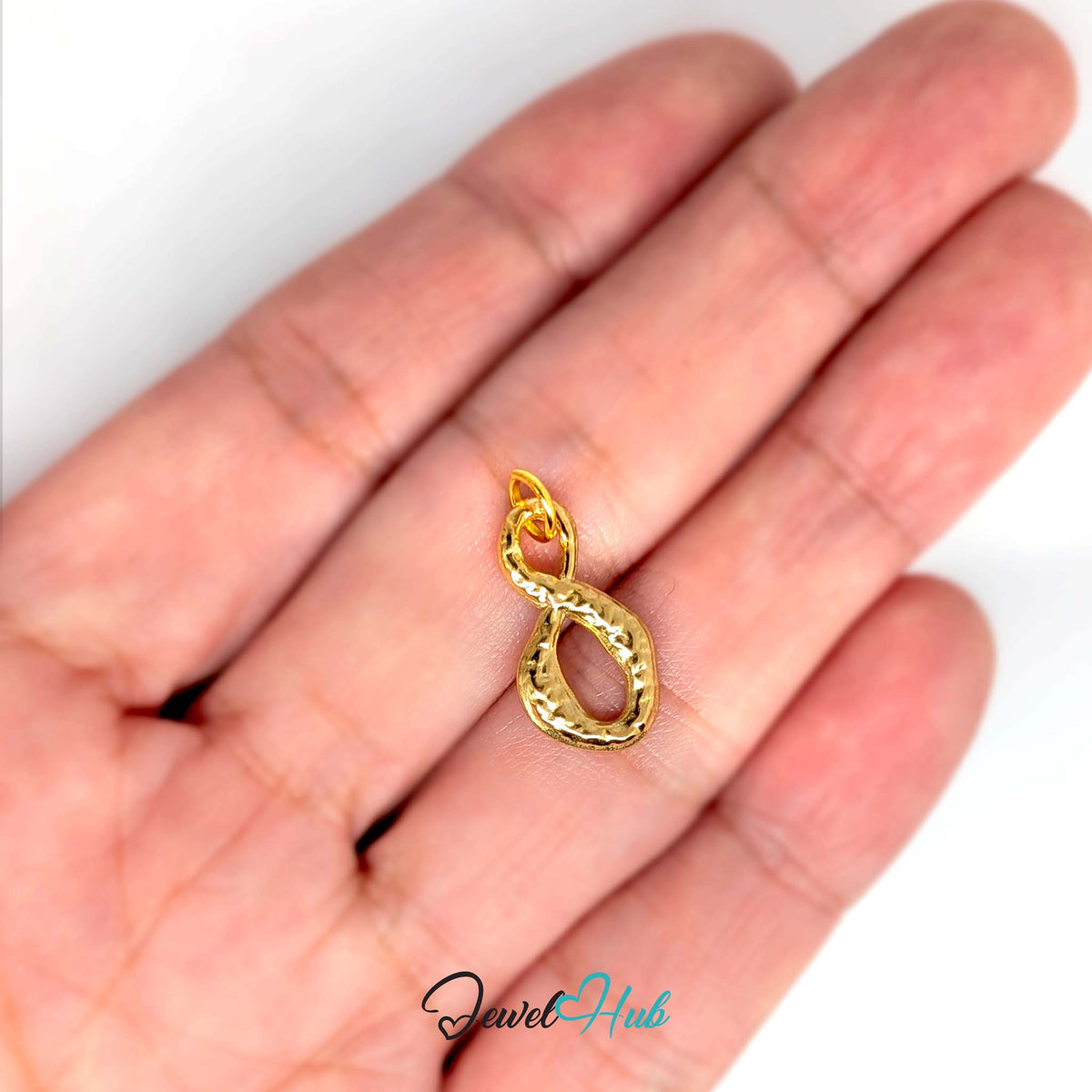 Textured infinity charm held in a hand to show its size - JewelHub