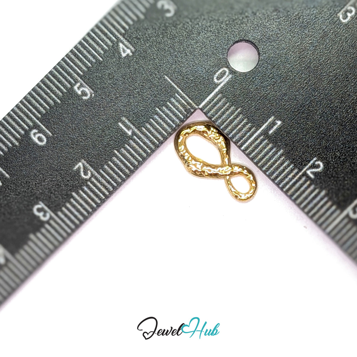 Textured infinity charm measured against a ruler at 9.6mm wide by 17.3mm tall - JewelHub