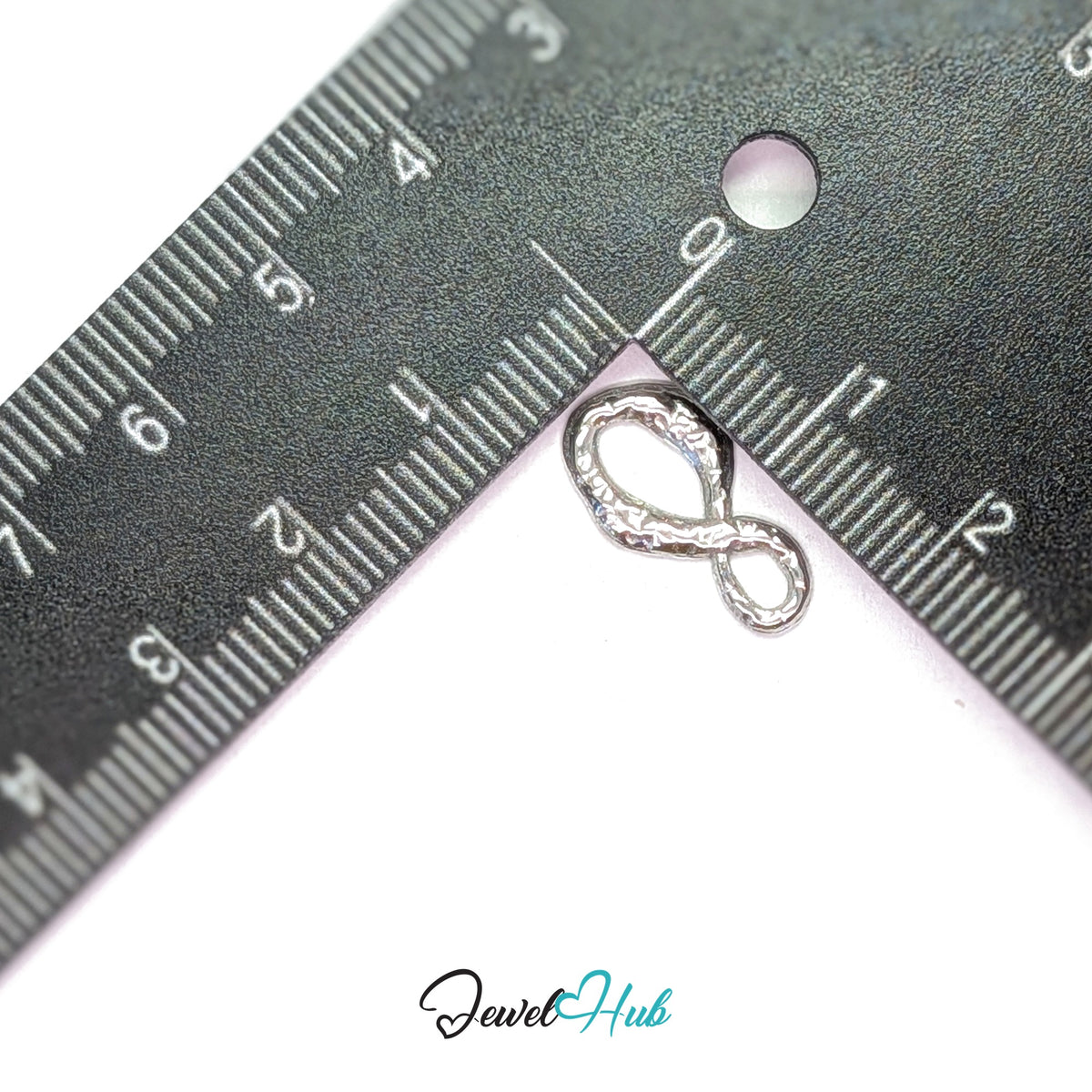 Textured infinity charm measured against a ruler at 9.6mm wide by 17.3mm tall - JewelHub