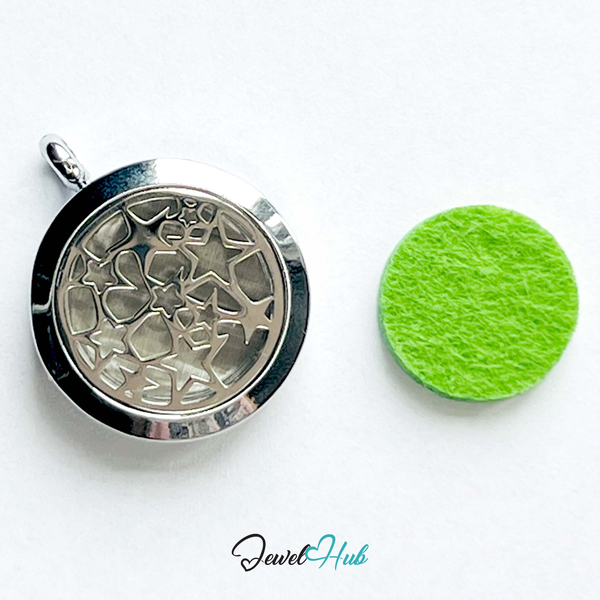 Silver pendant with intricate design on a white background, next to a green round object.
