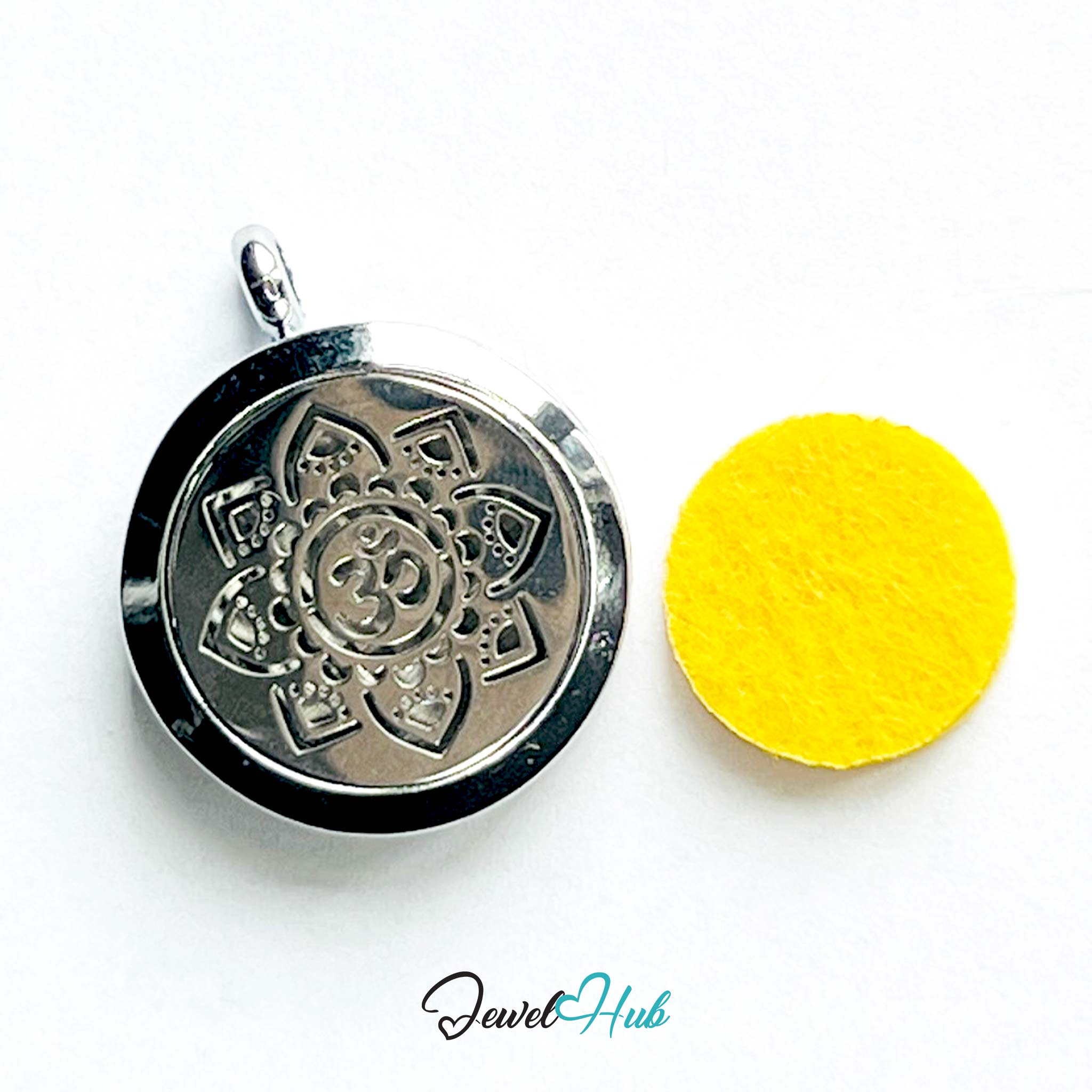 Silver pendant with intricate design on a white background, next to a yellow round object.