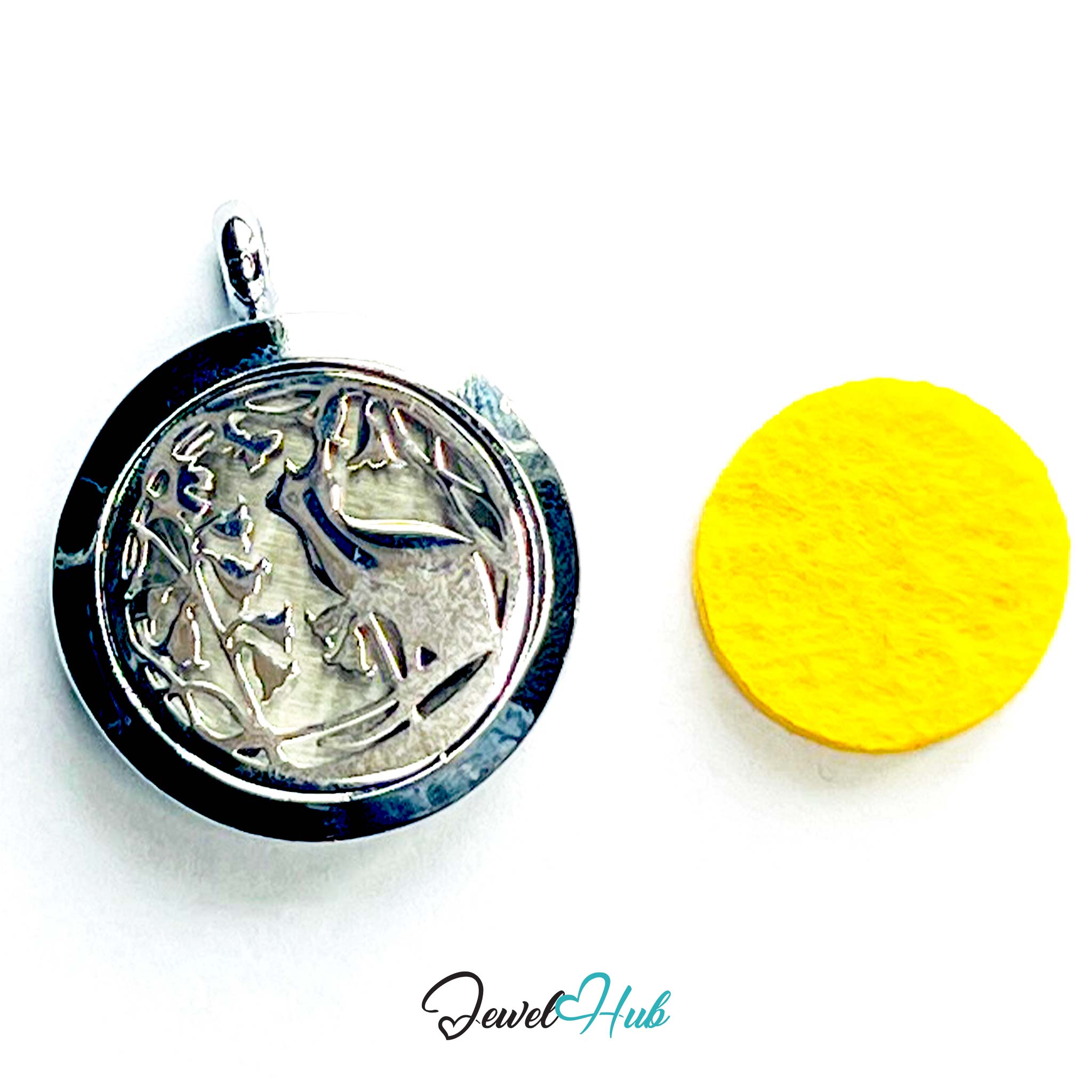 Silver pendant with intricate design on a white background, next to a yellow round object.